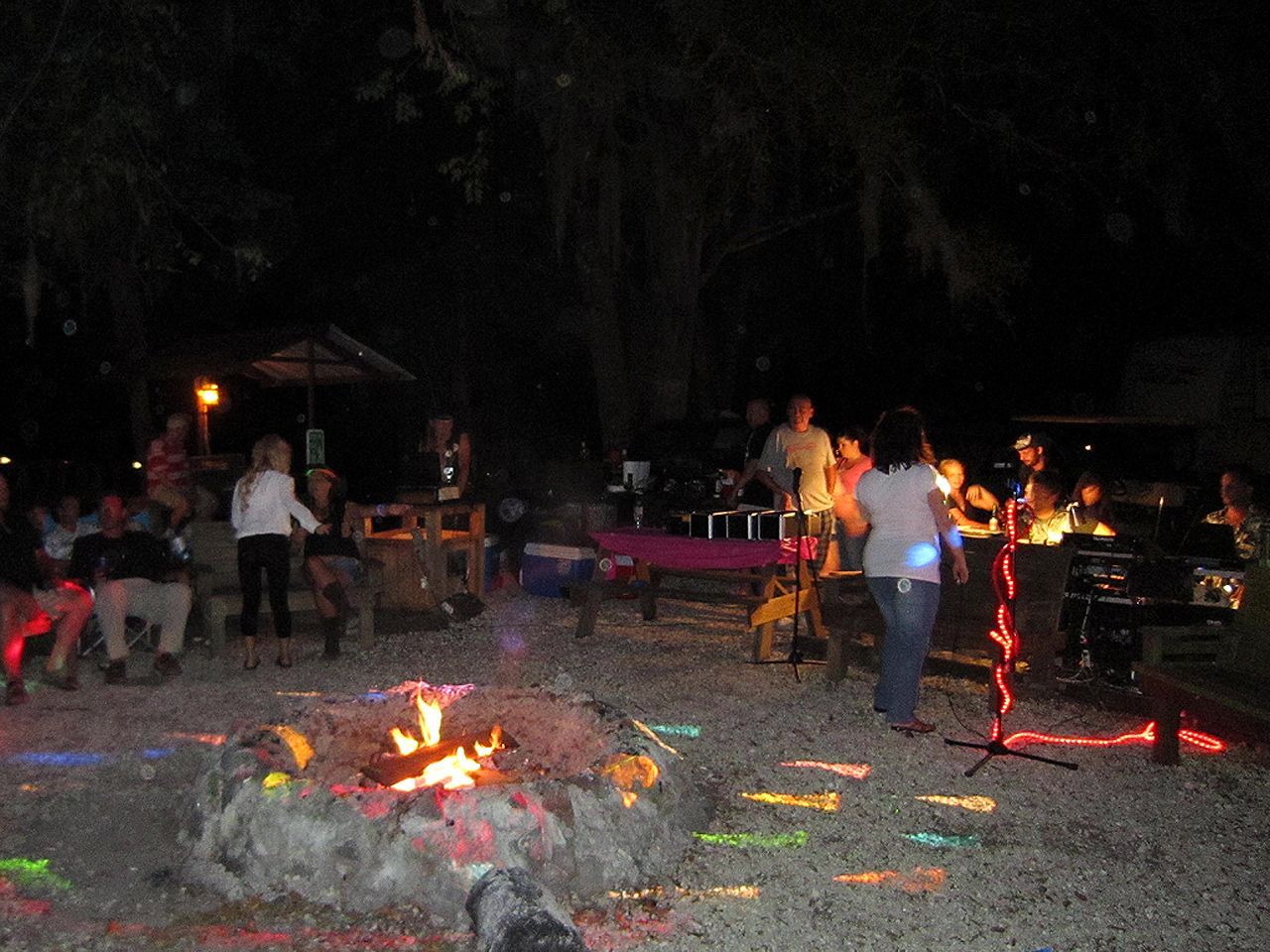 a group of people are standing around a fire pit at night .