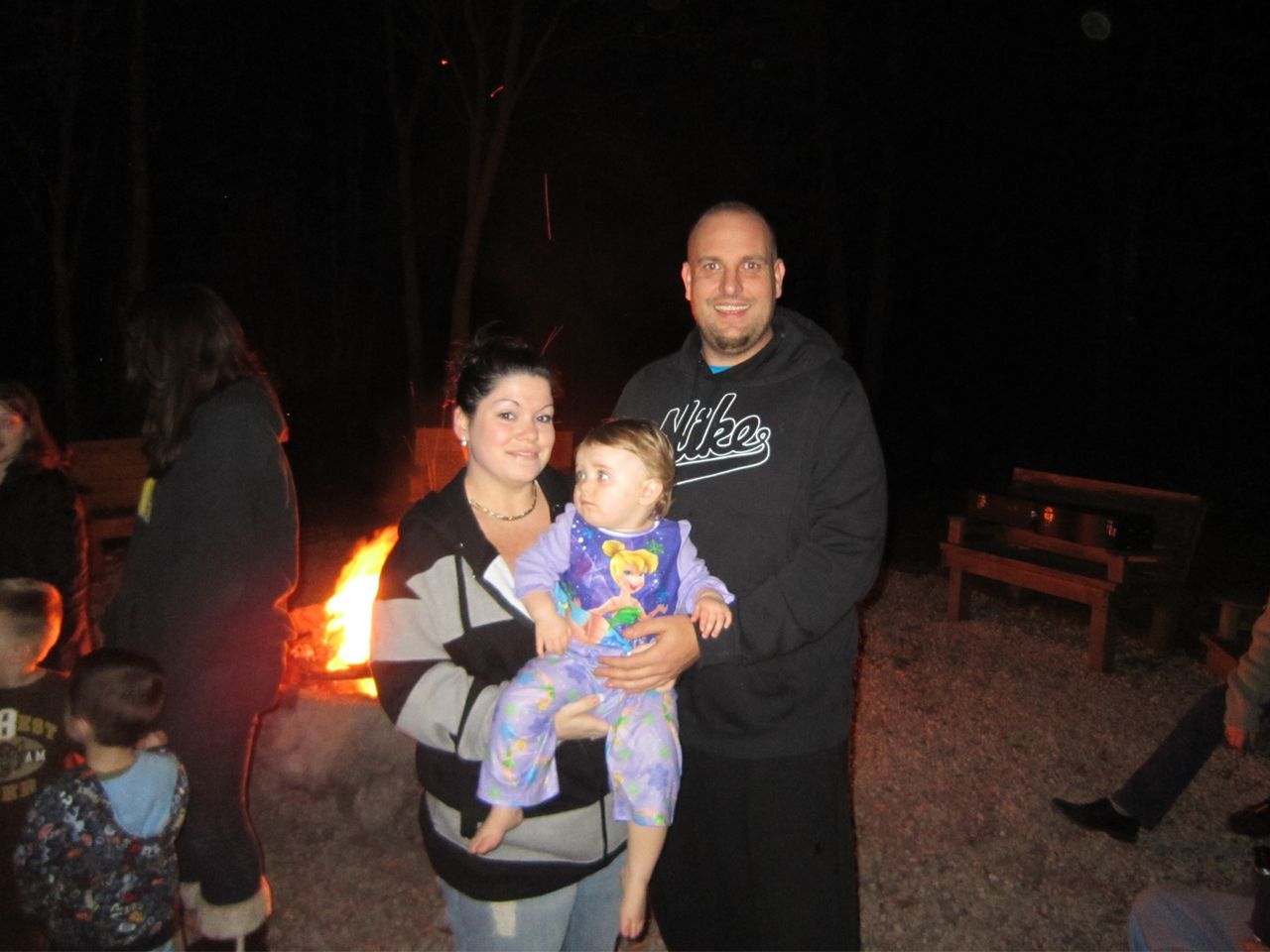 a man and woman holding a baby in front of a fire
