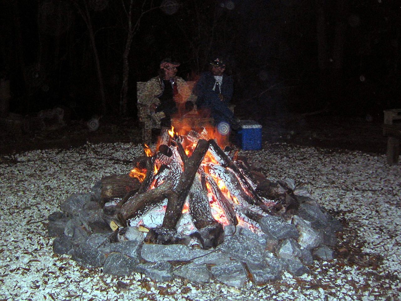 two people are sitting around a campfire at night
