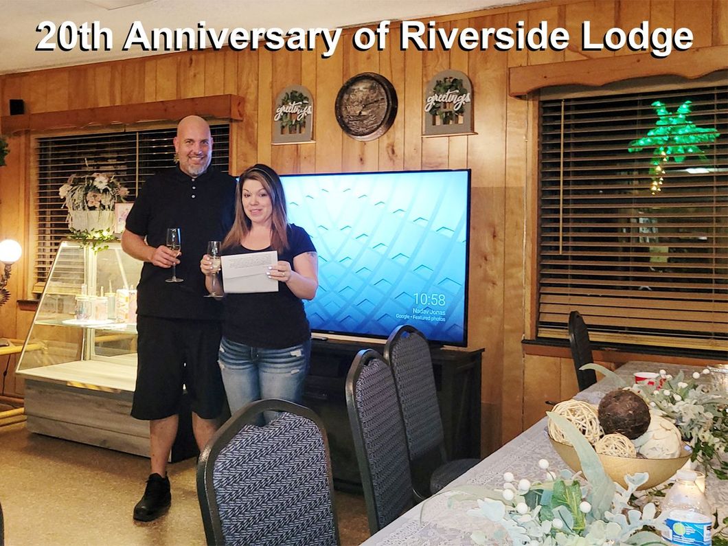 a man and a woman are standing in a room with a sign that says 20th anniversary of riverside lodge