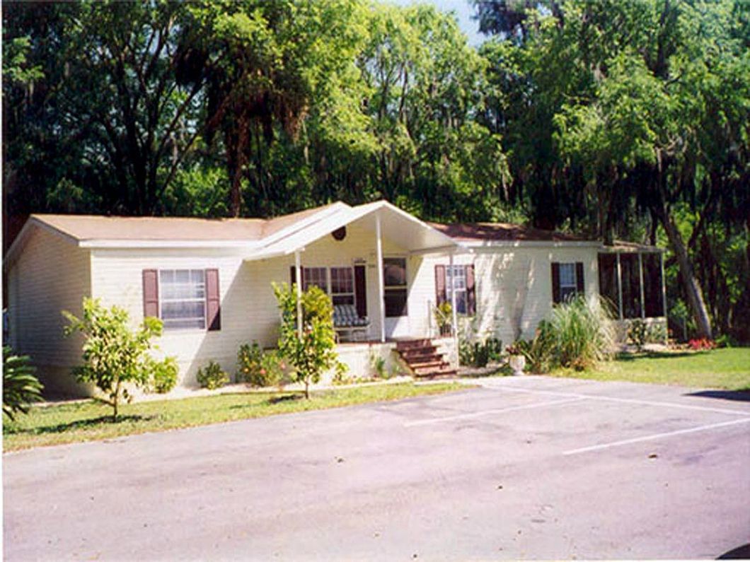a white mobile home with a porch and trees in the background