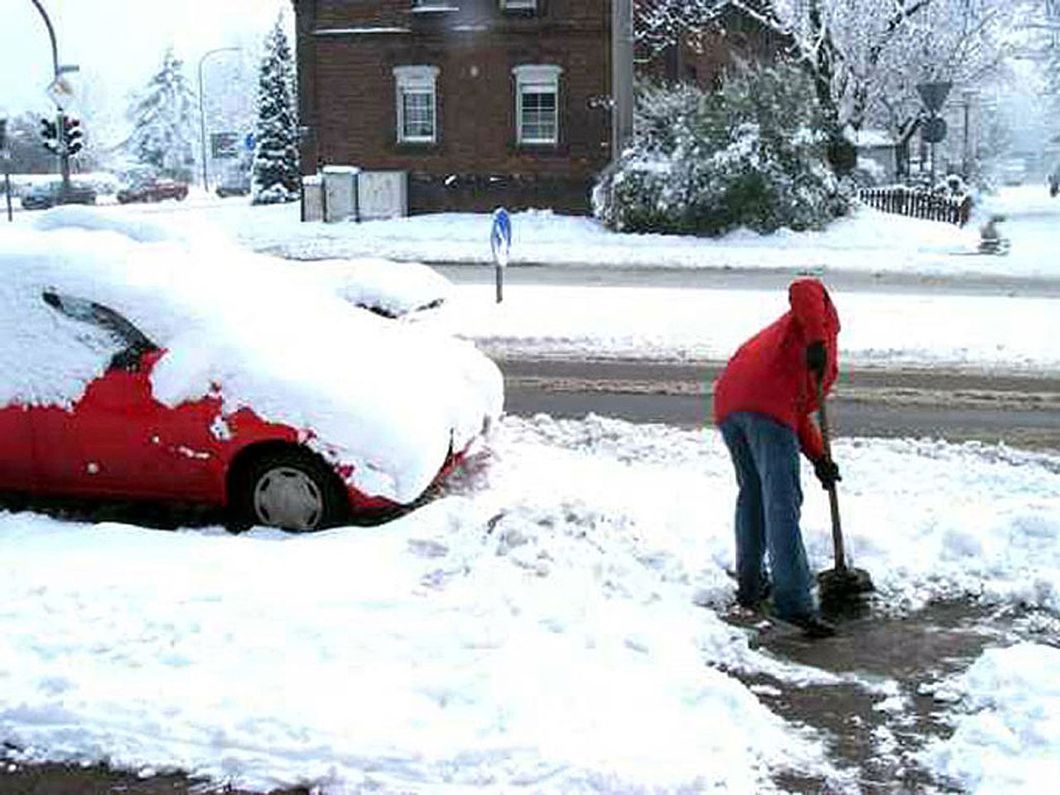 a person is shoveling snow in front of a red car