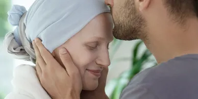 A man is kissing a woman with cancer on the forehead.