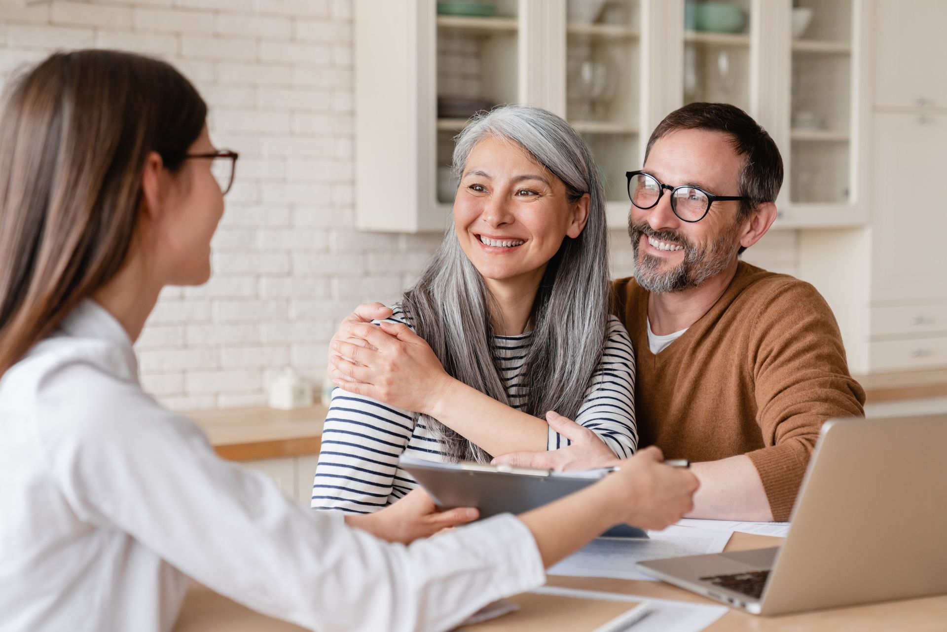A financial advisor consults with a smiling couple at a table with papers and a laptop.