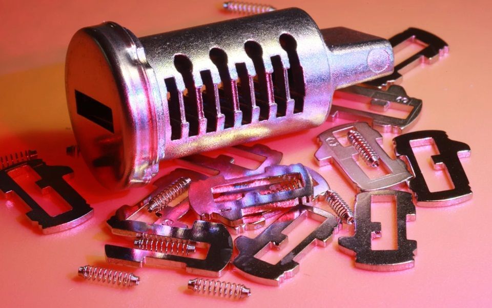 A lock tumbler with pins and springs on a pink surface.