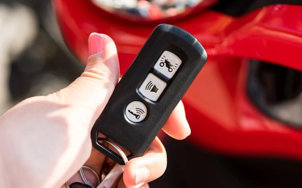 A hand holding a smart key with a red car in the background.