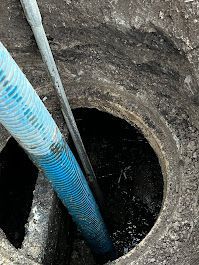A blue hose is being used to pump water into a hole in the ground.