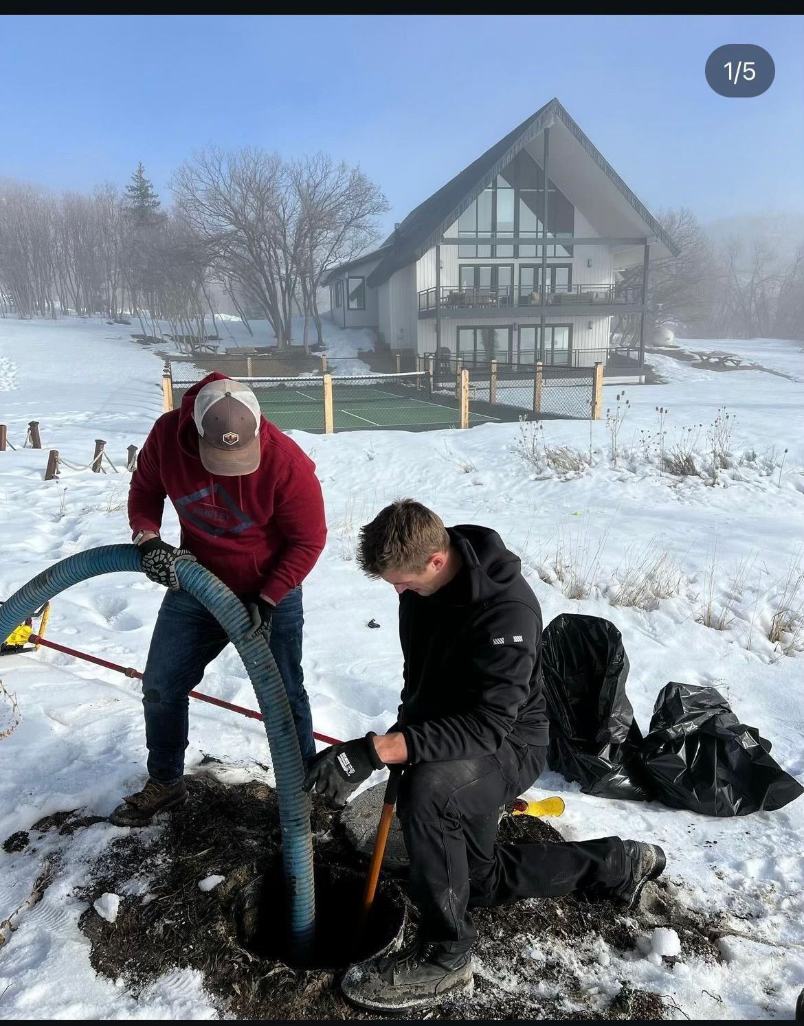 Two men are working in the snow in front of a house.