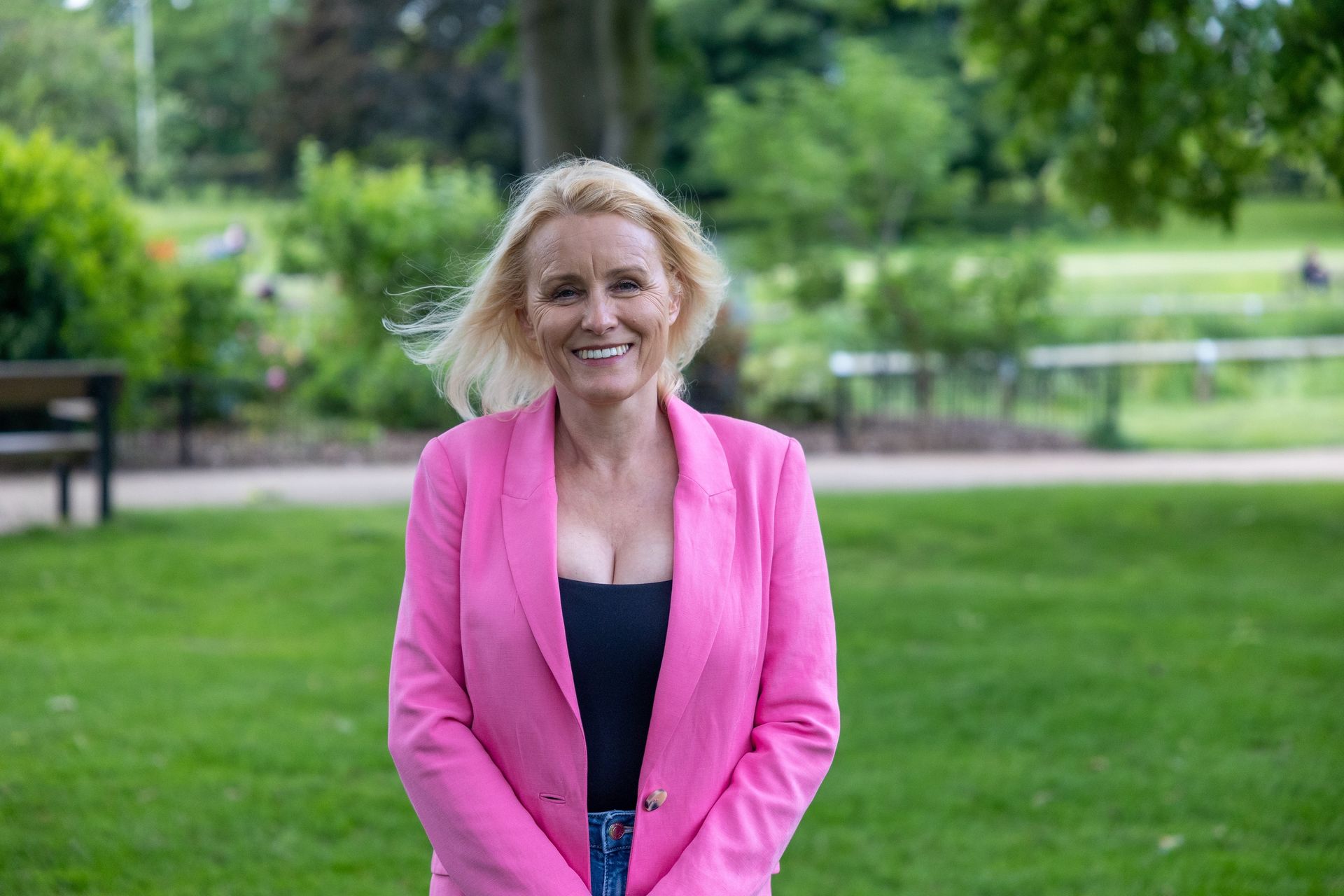 A woman in a pink jacket is standing in a park.