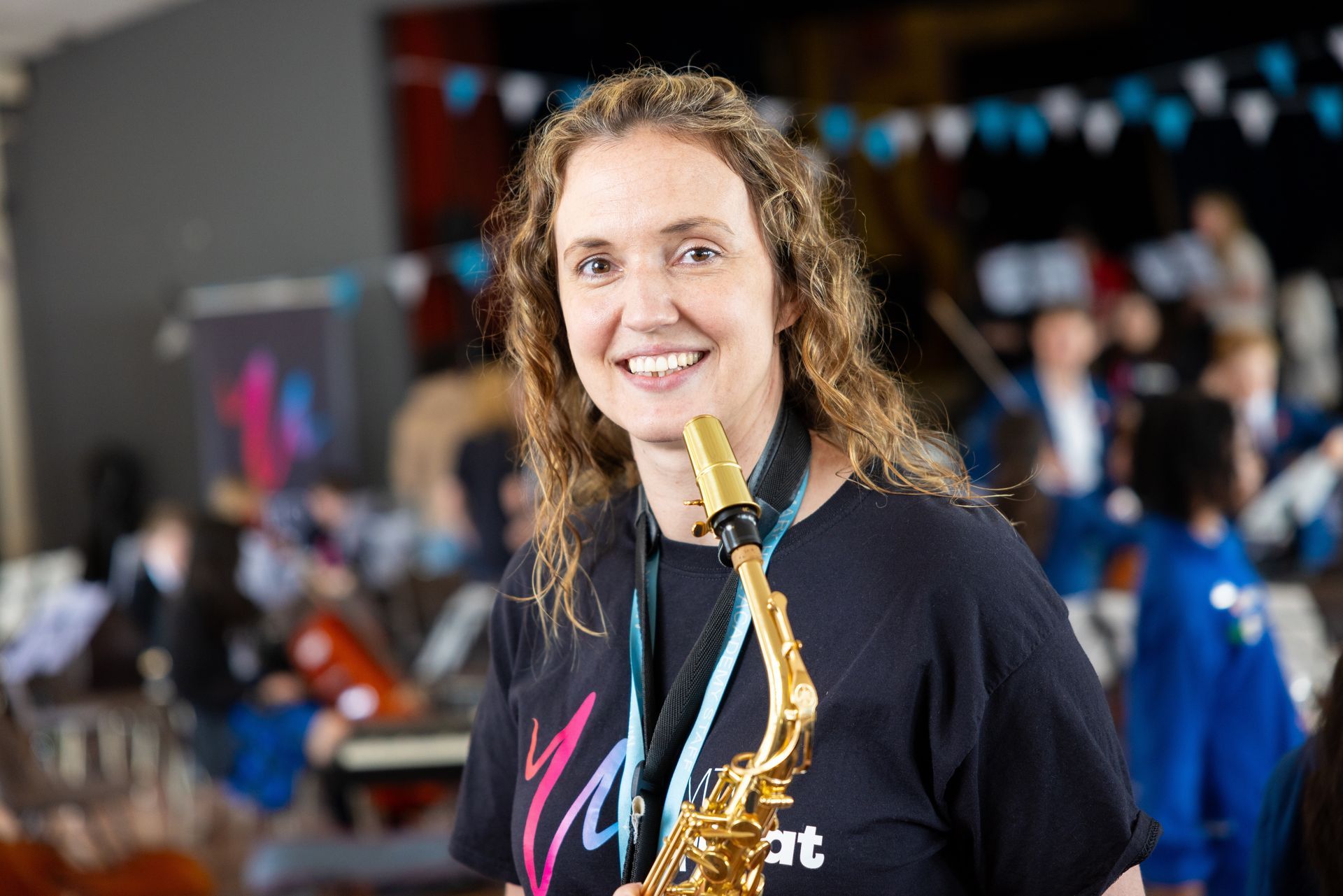 A woman in a black shirt is holding a saxophone and smiling.