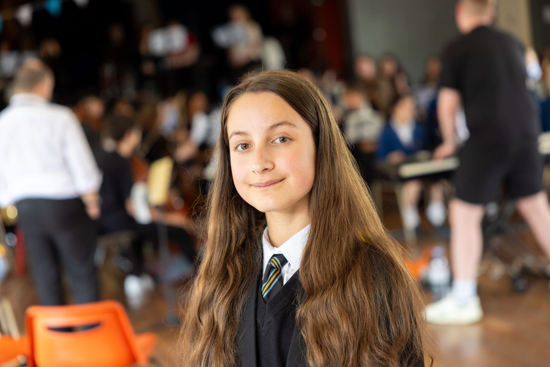 A young girl in a school uniform is standing in front of a crowd of people.