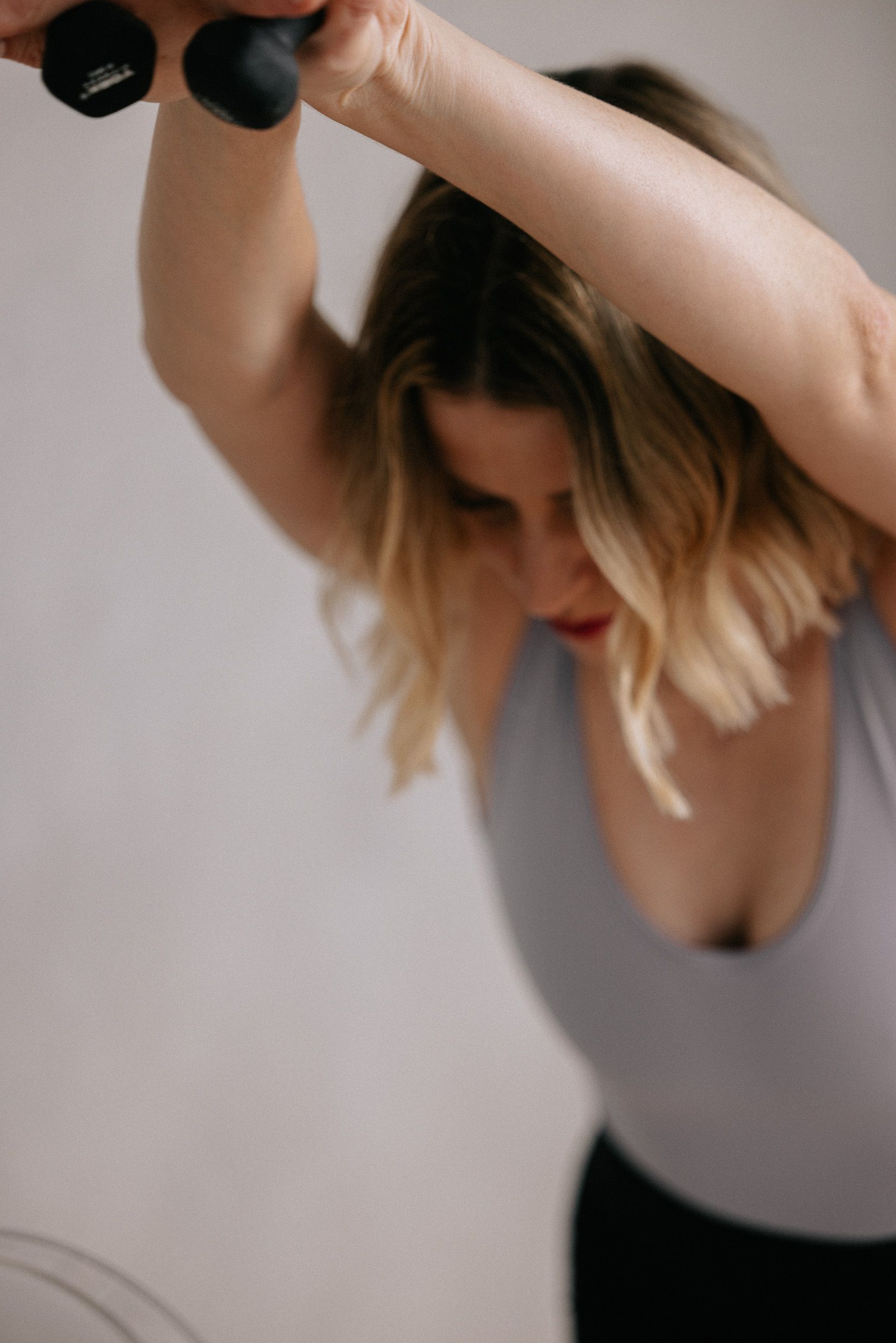 A woman is holding a pair of dumbbells over her head.
