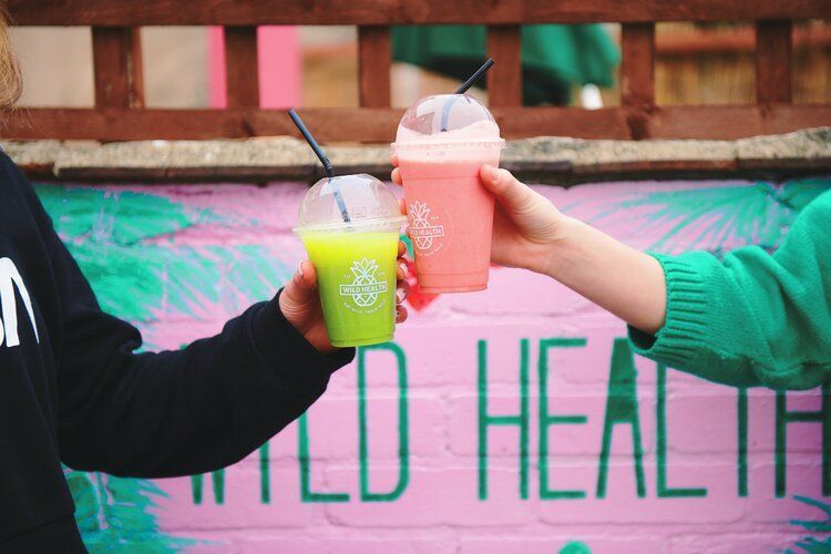 two people are toasting with smoothies in front of a mural .