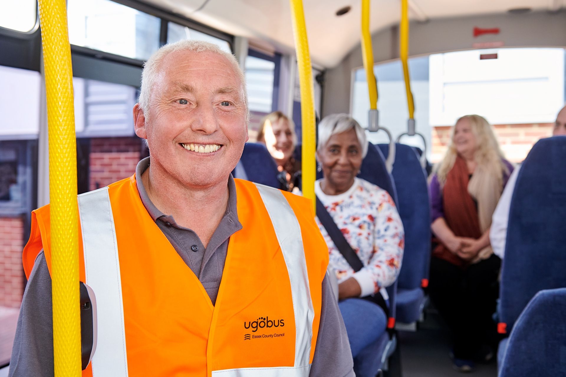 A man in an orange vest is sitting on a bus.