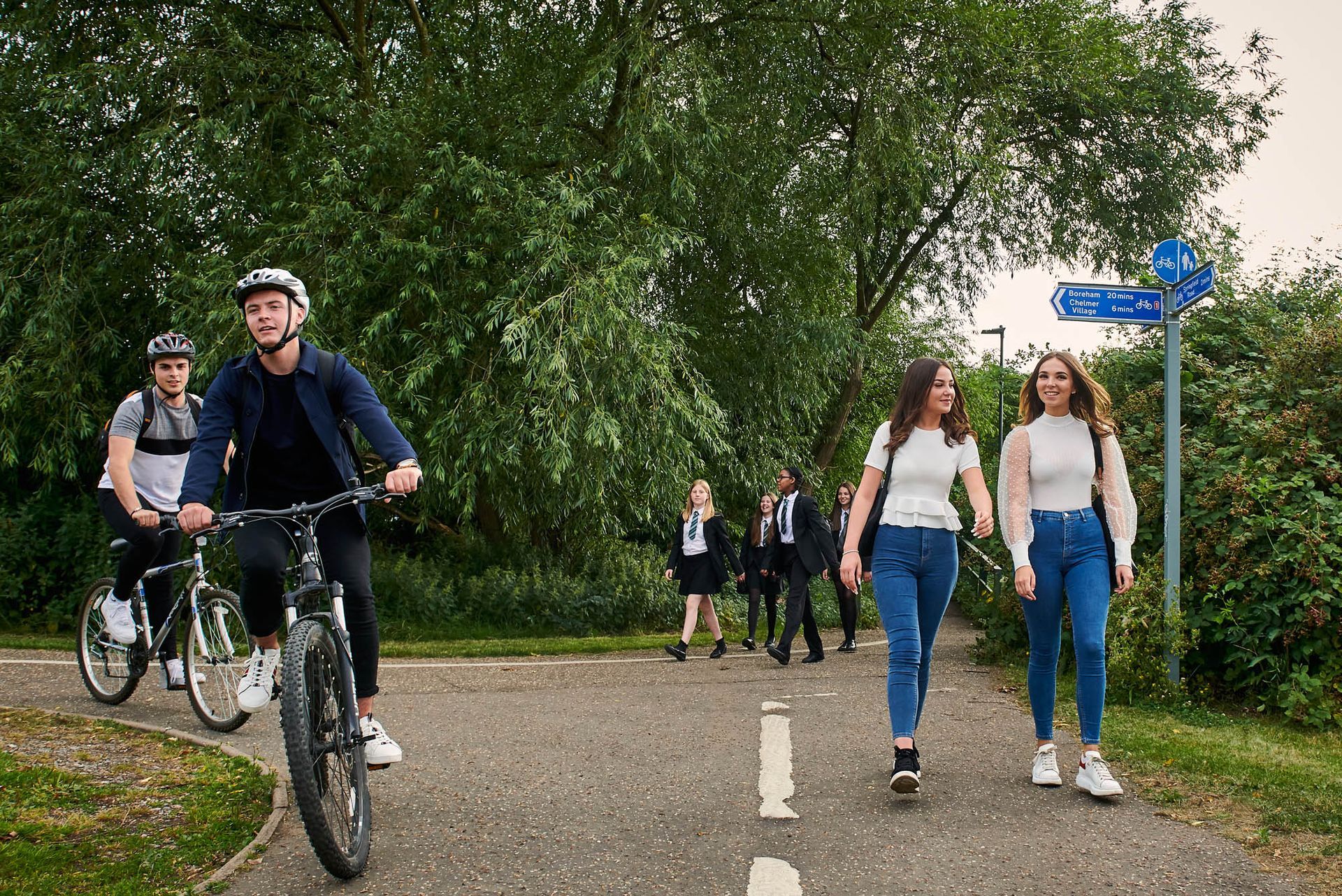 A group of young people are walking and riding bikes on a path.