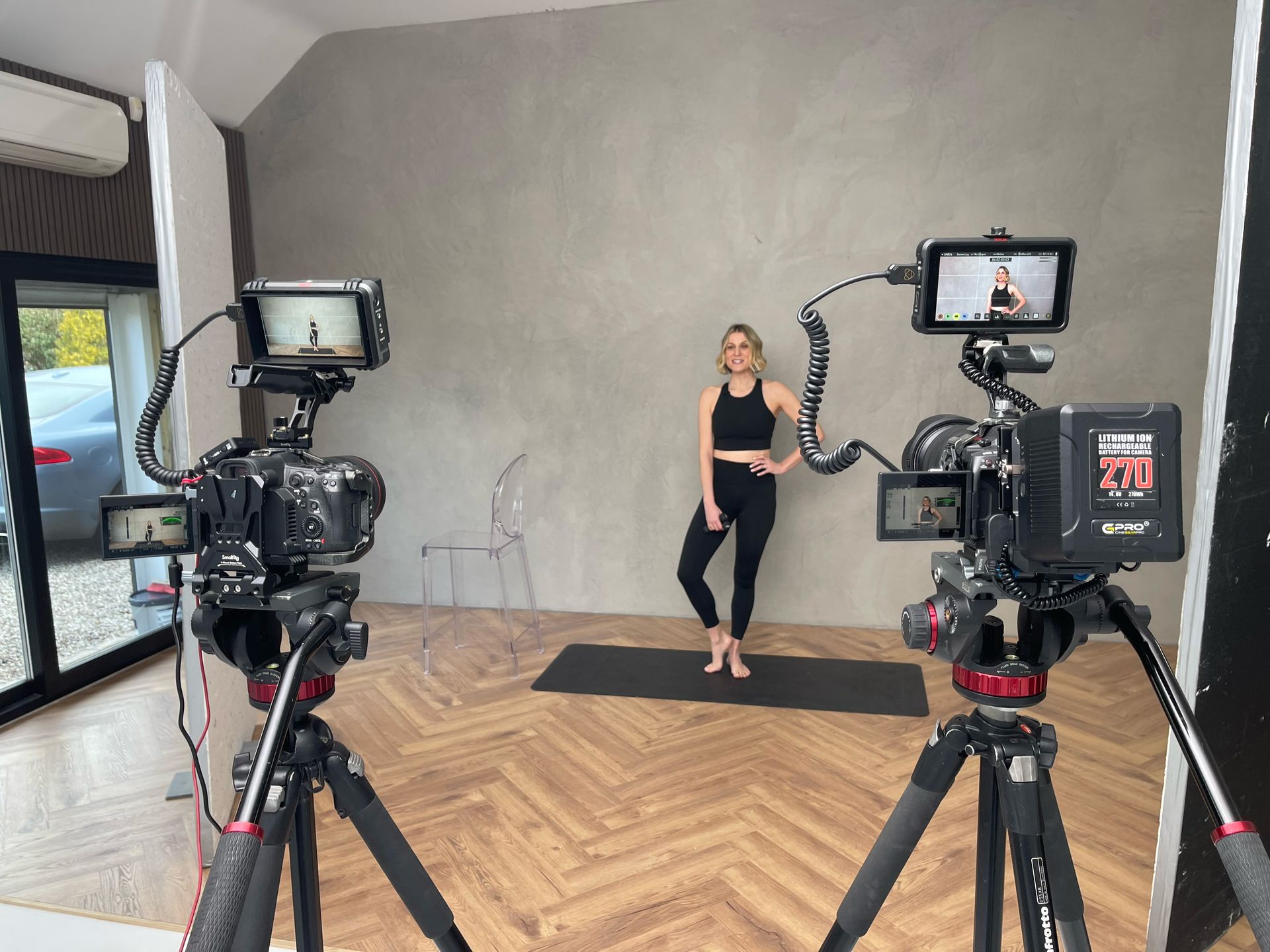 A woman is standing on a yoga mat in front of two cameras.
