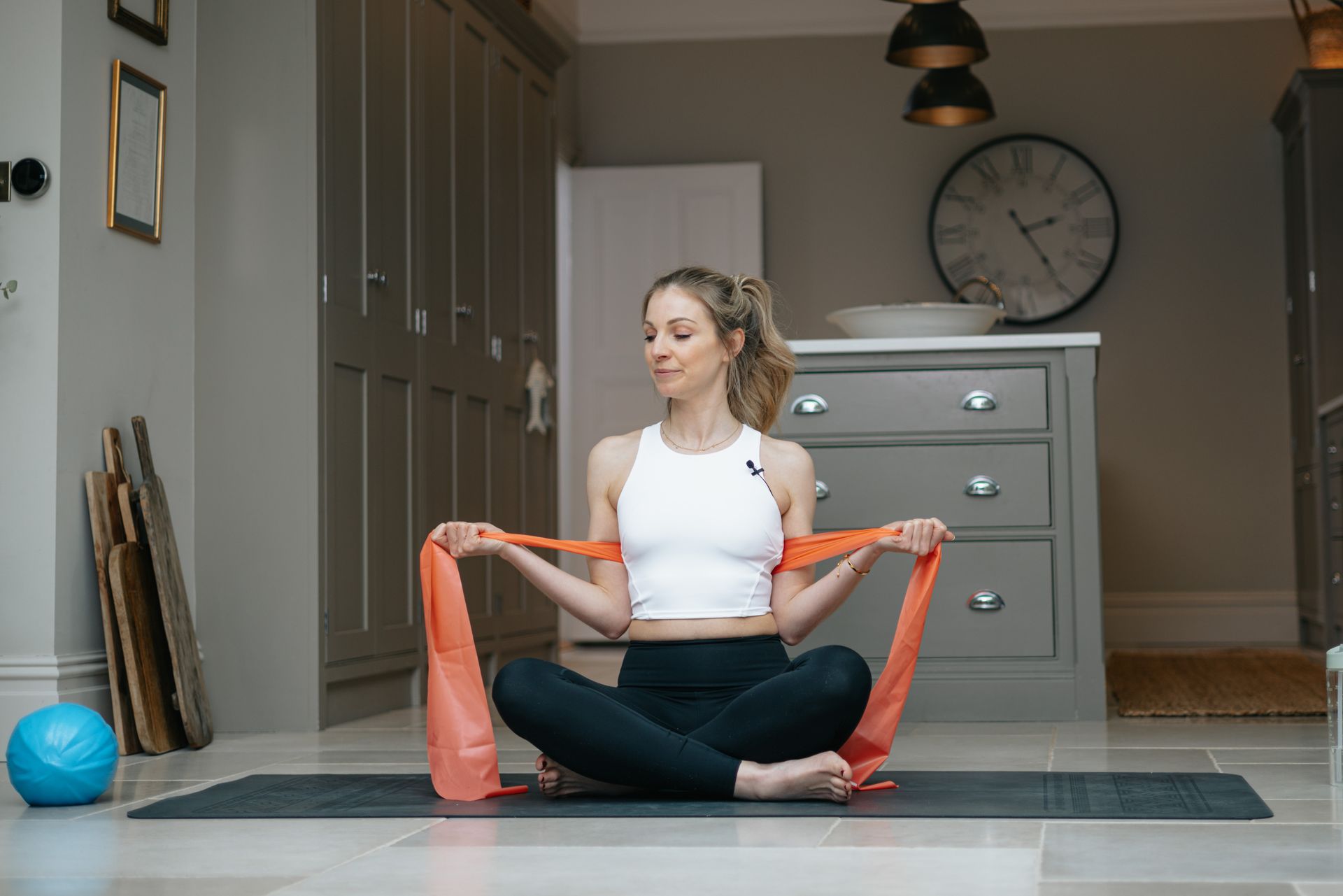 A woman is sitting on a yoga mat with a resistance band around her neck.