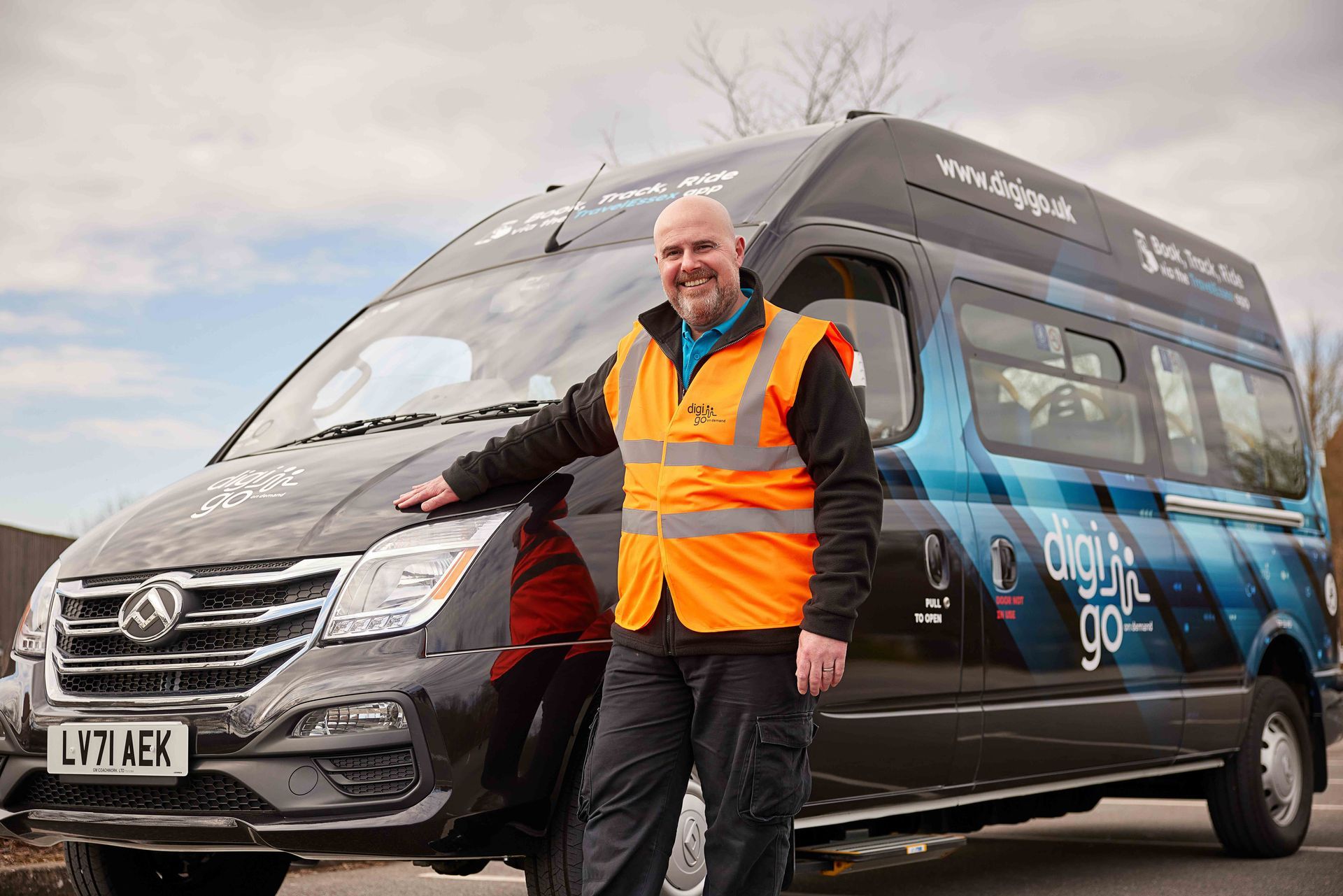 A man in an orange vest is standing next to a black van.