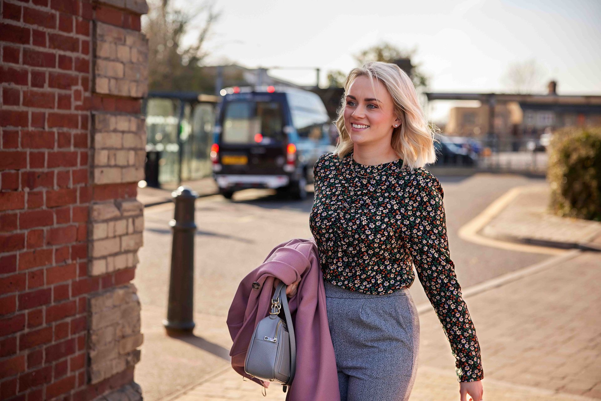A woman is walking down a sidewalk next to a brick wall.