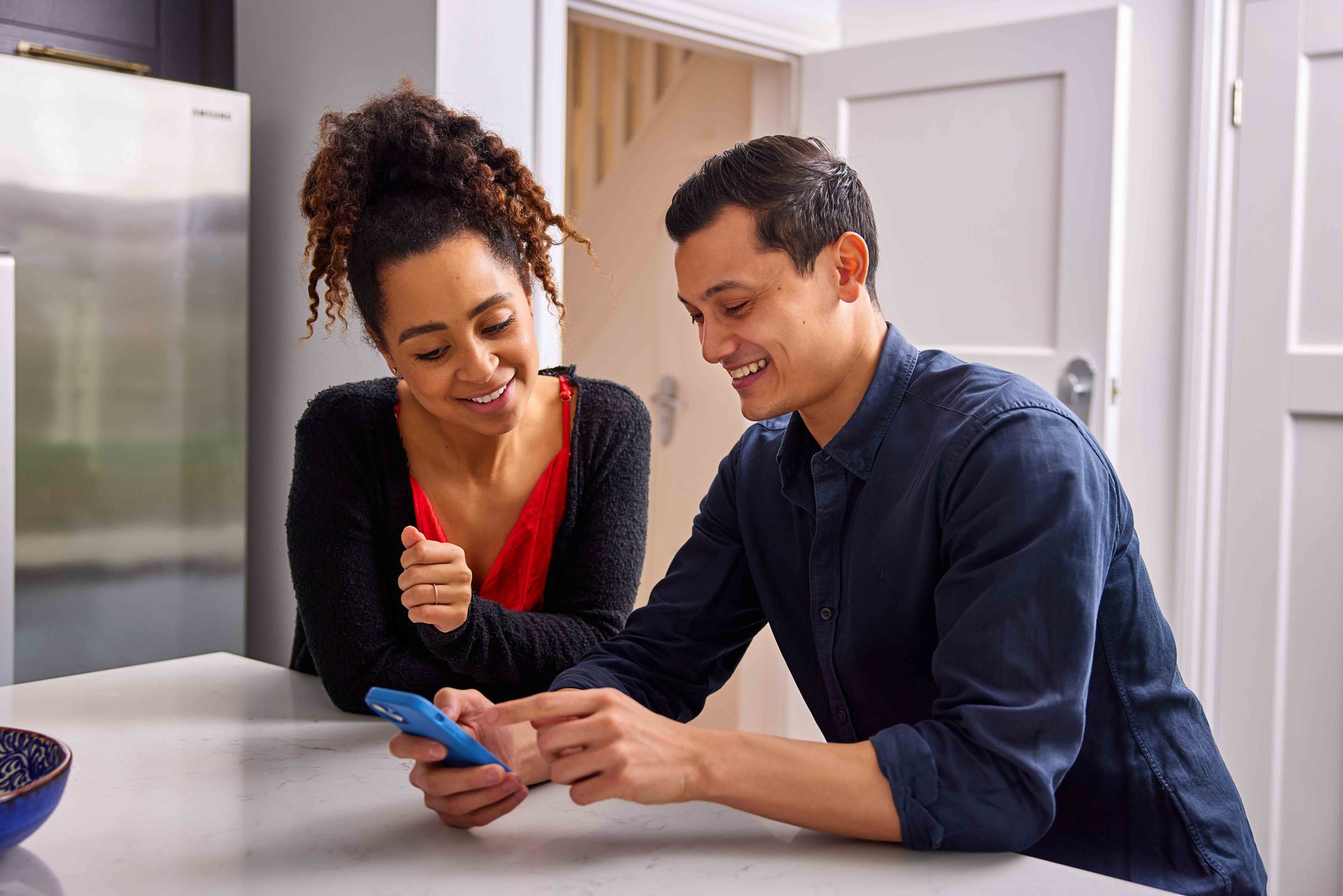 A man and a woman are sitting at a table looking at a cell phone.