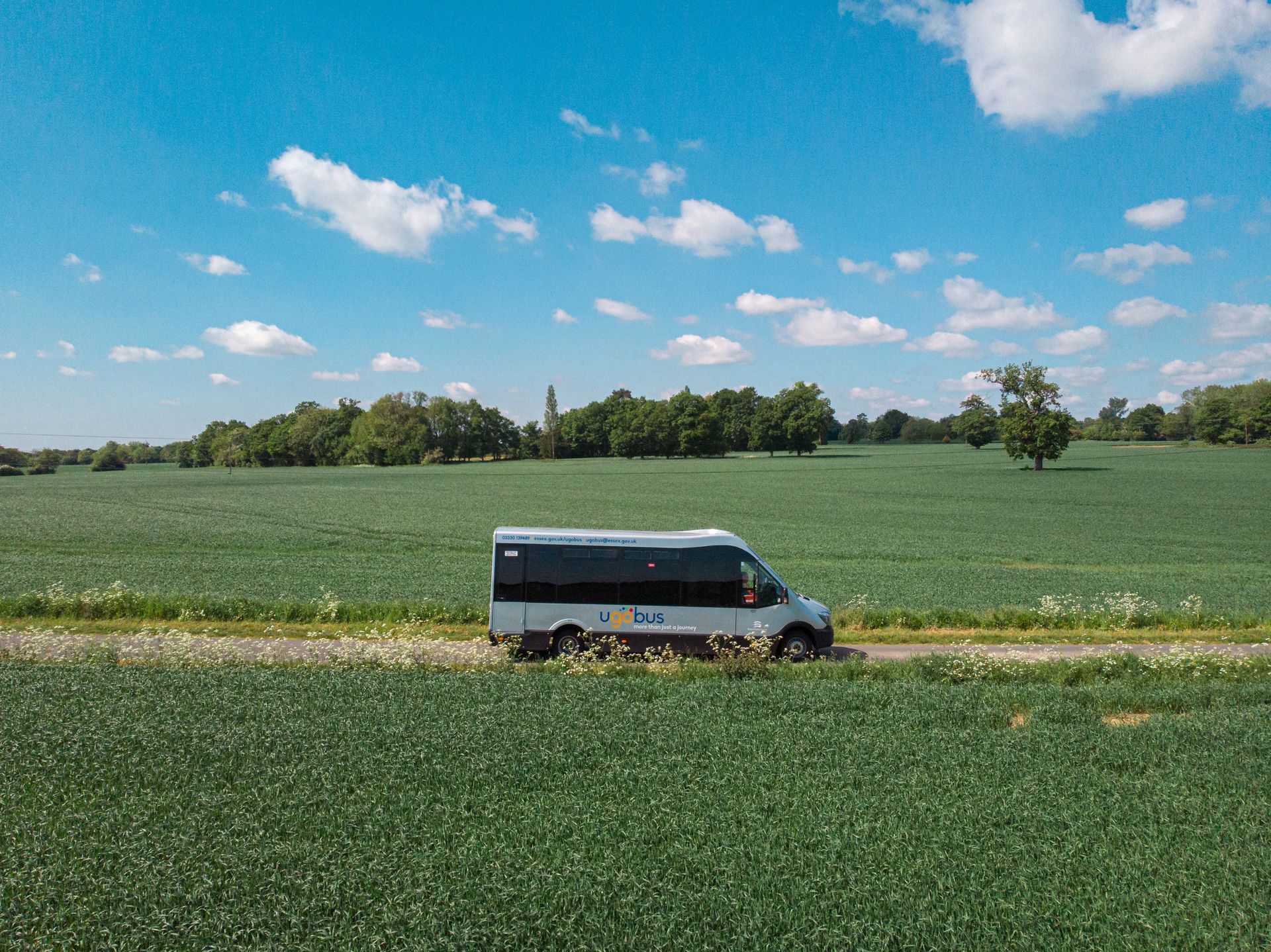 A white van is driving down a dirt road in a field.