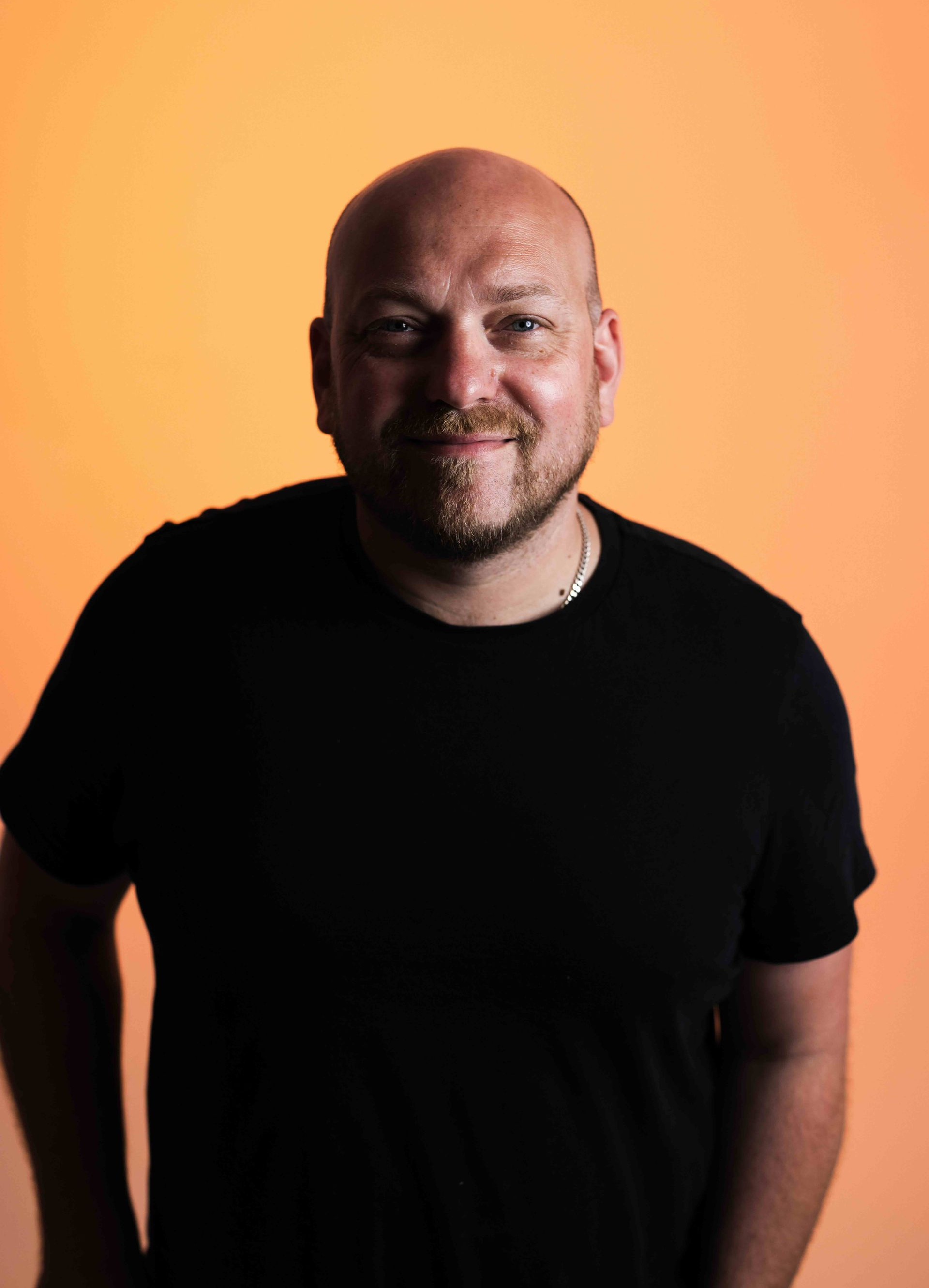 A bald man with a beard is wearing a black shirt and looking at the camera.