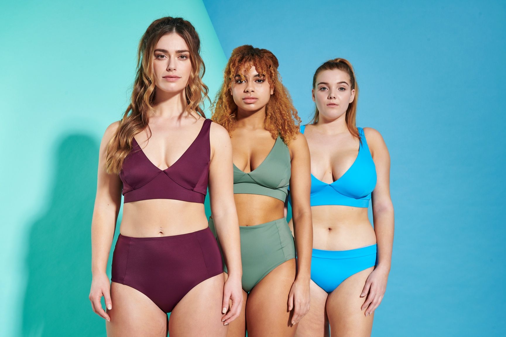 Three women in bikinis are standing next to each other on a blue background.