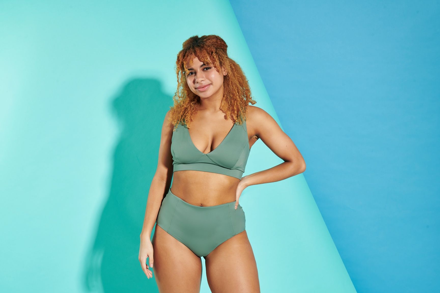 A woman in a bikini is standing in front of a blue wall.