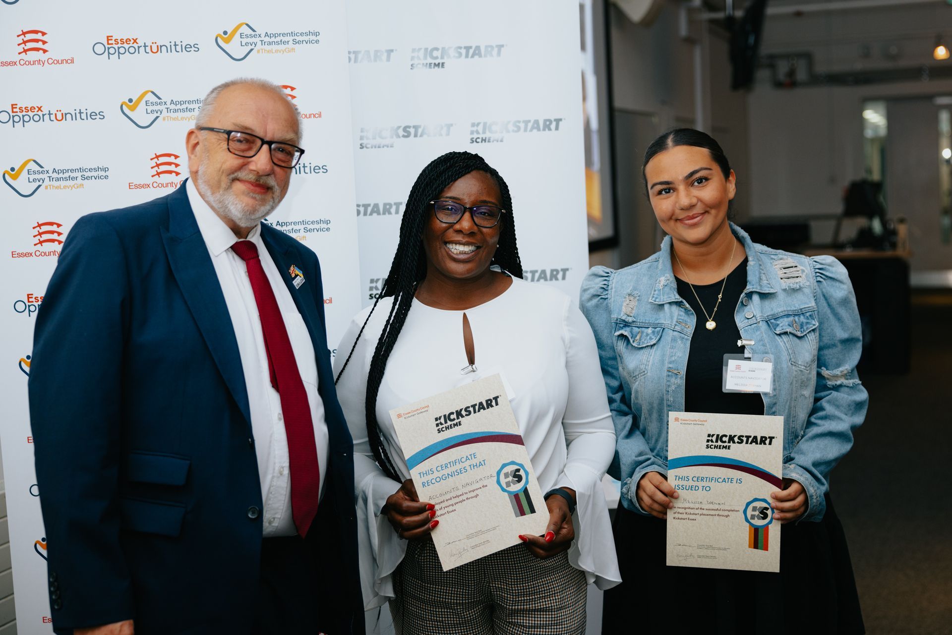 A man in a suit and tie is standing next to two women holding certificates.