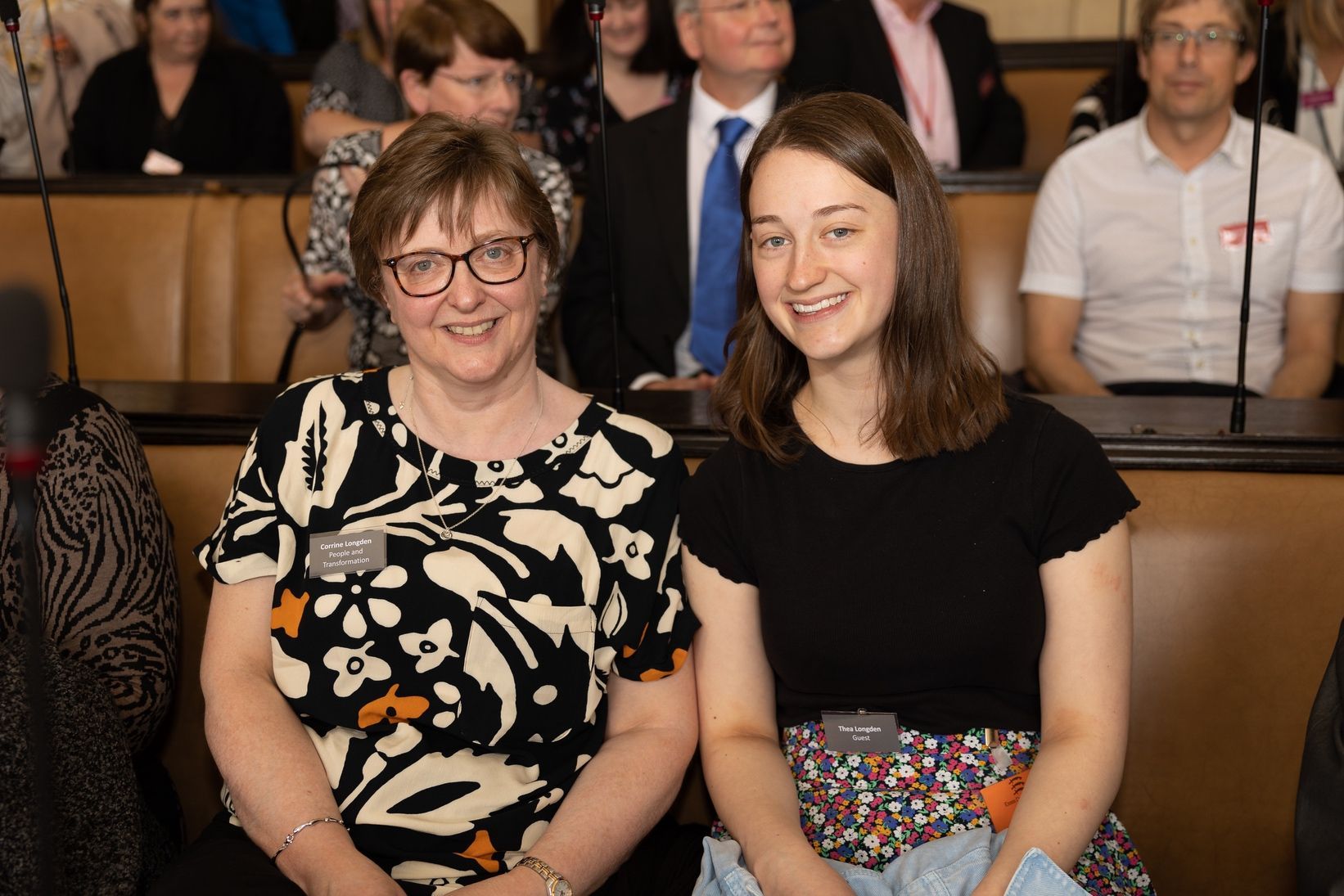 Two women are sitting next to each other in front of a crowd of people.