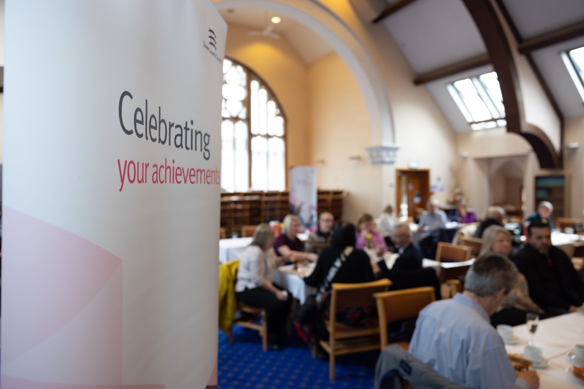 People sitting at tables in a room with a sign that says celebrating your achievement