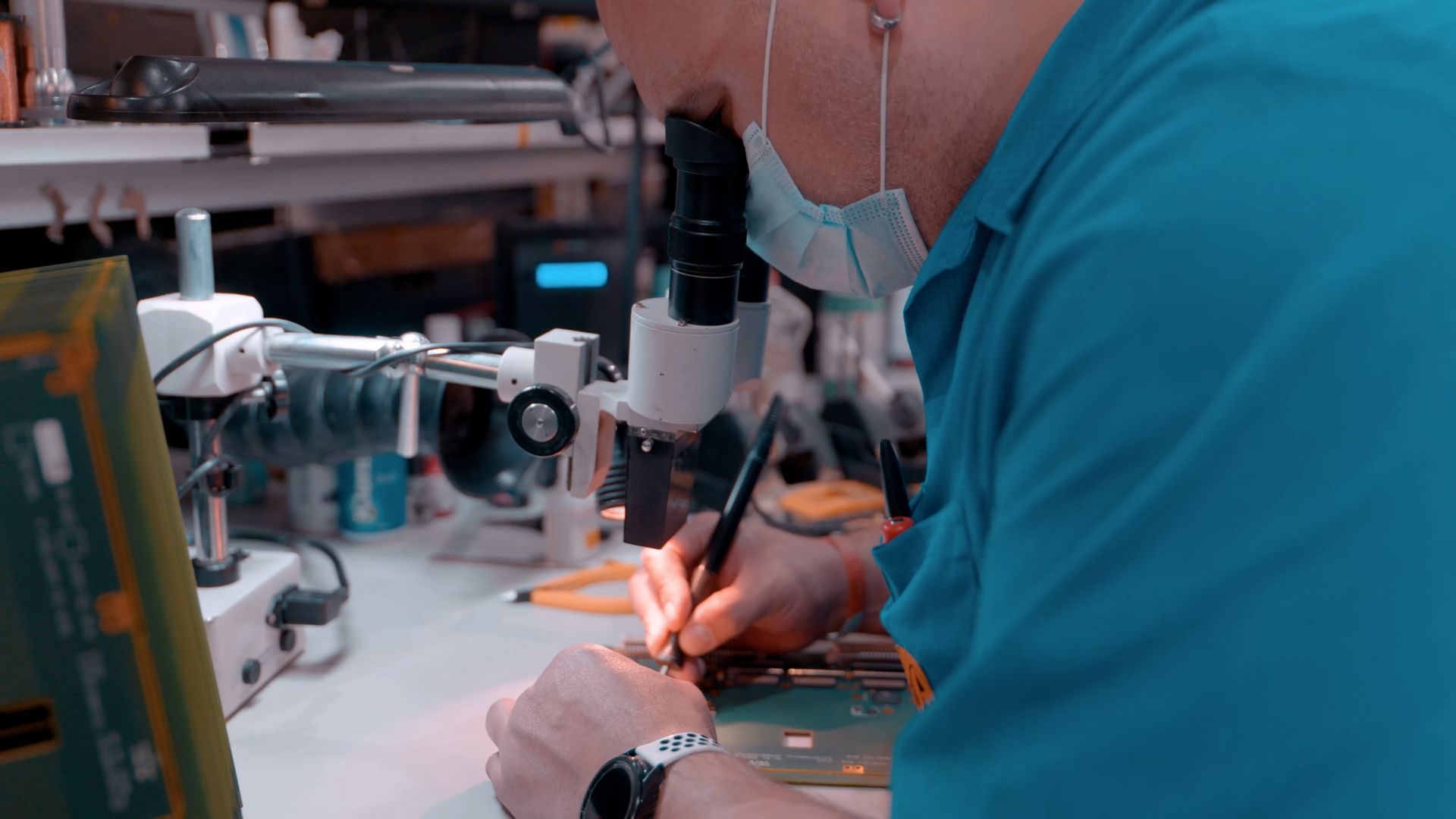 A man is working in a lab with a microscope and a soldering iron.