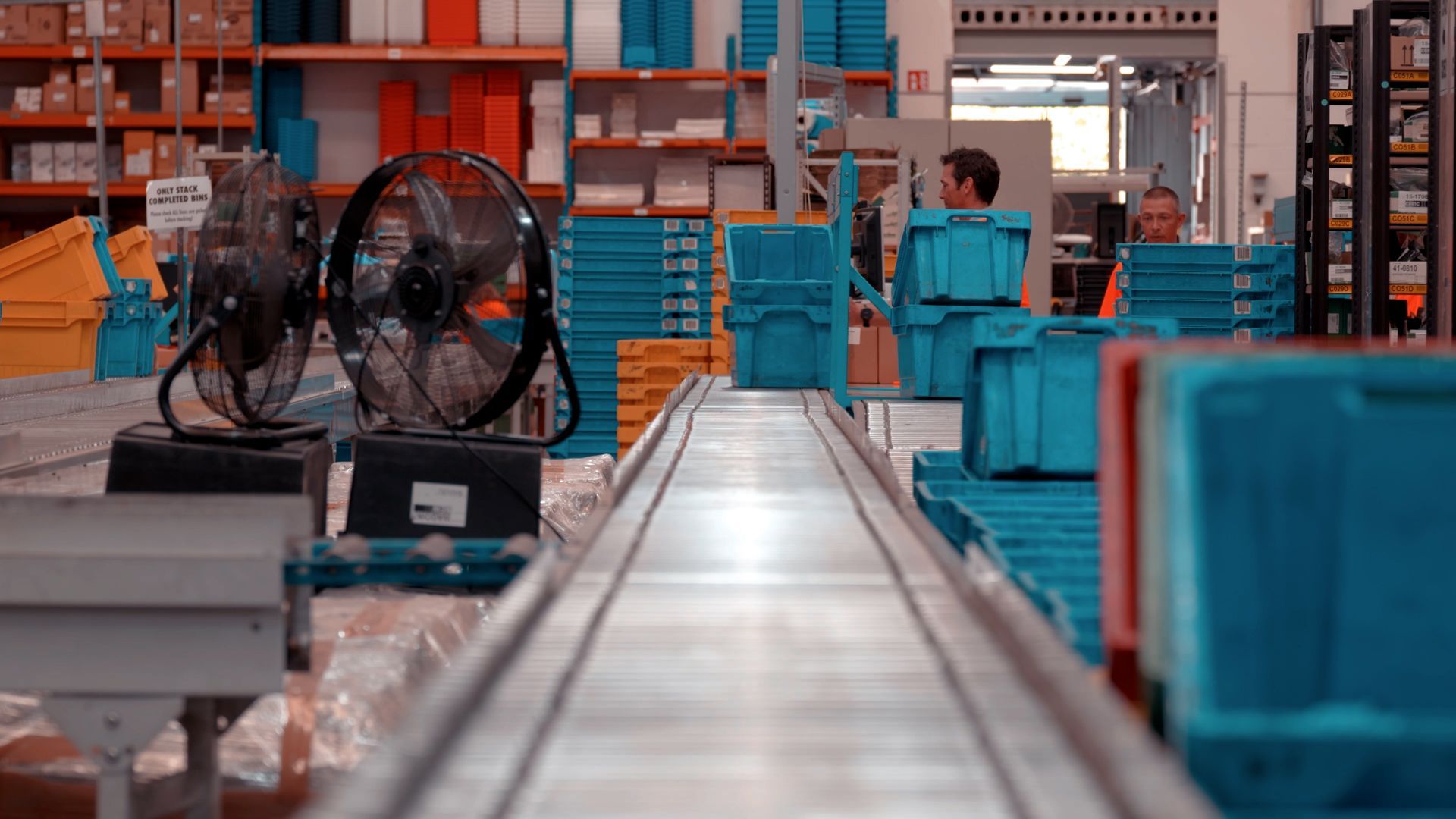 Two fans are sitting on top of a conveyor belt in a warehouse.