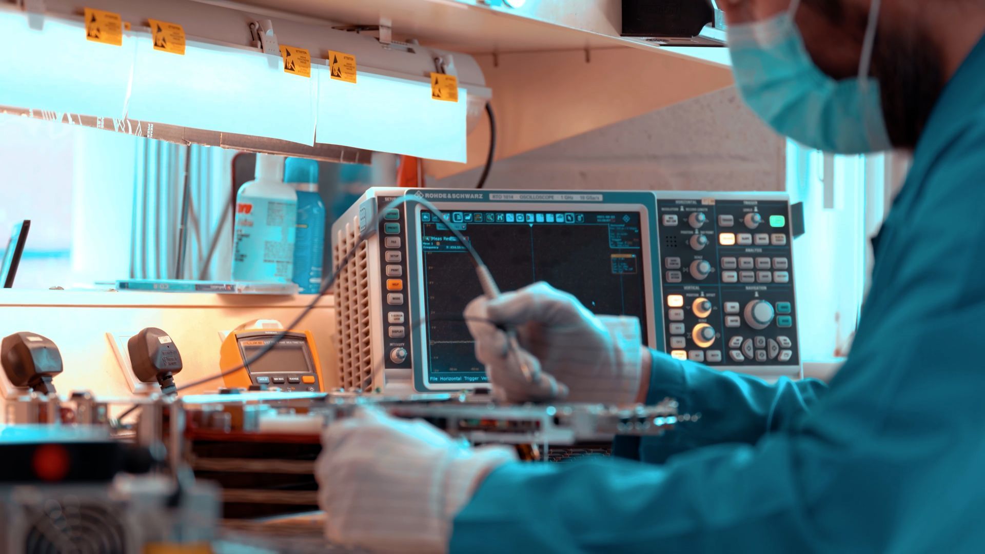A man wearing a mask and gloves is working on a machine in a lab.