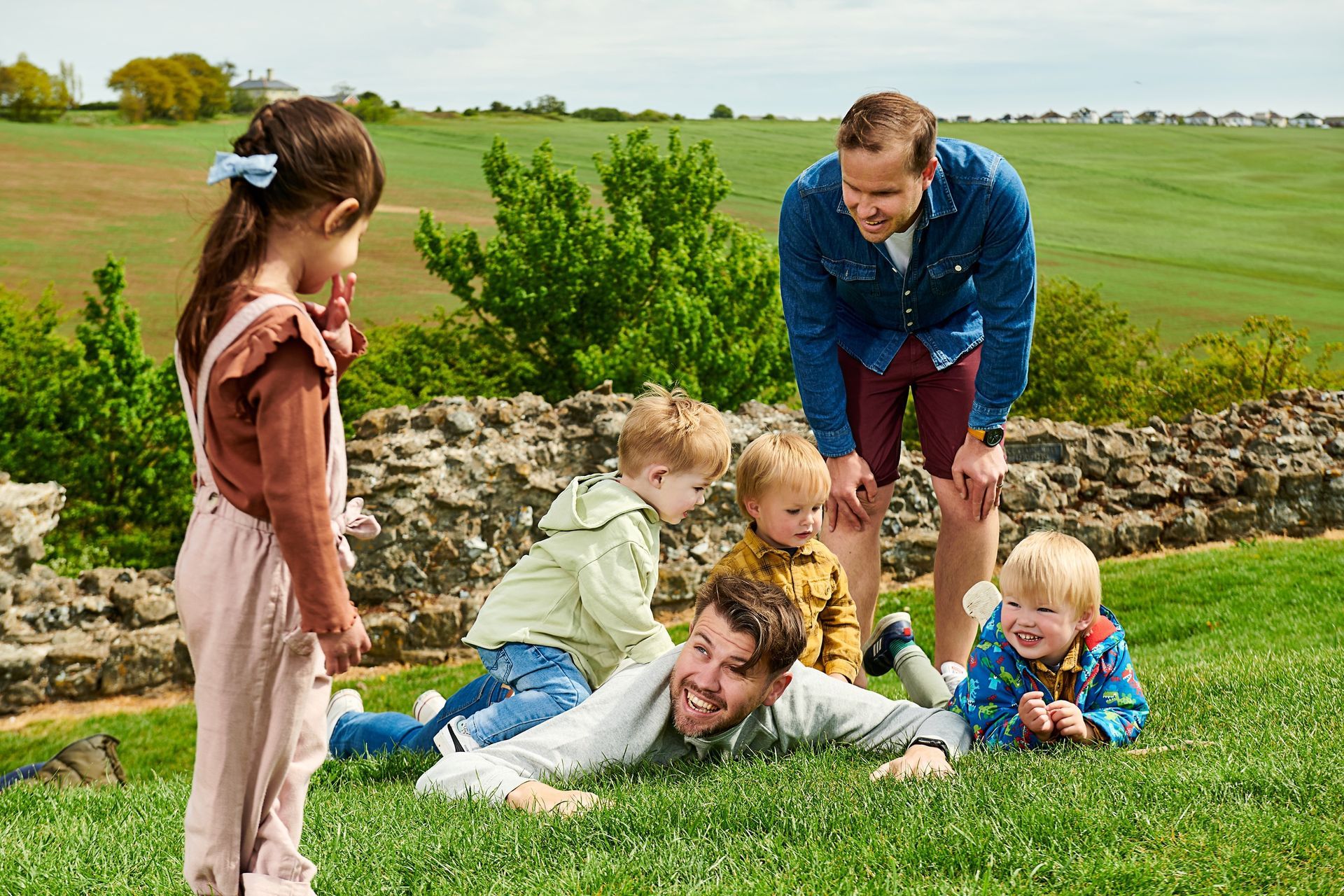 A man is laying on the grass with three children.