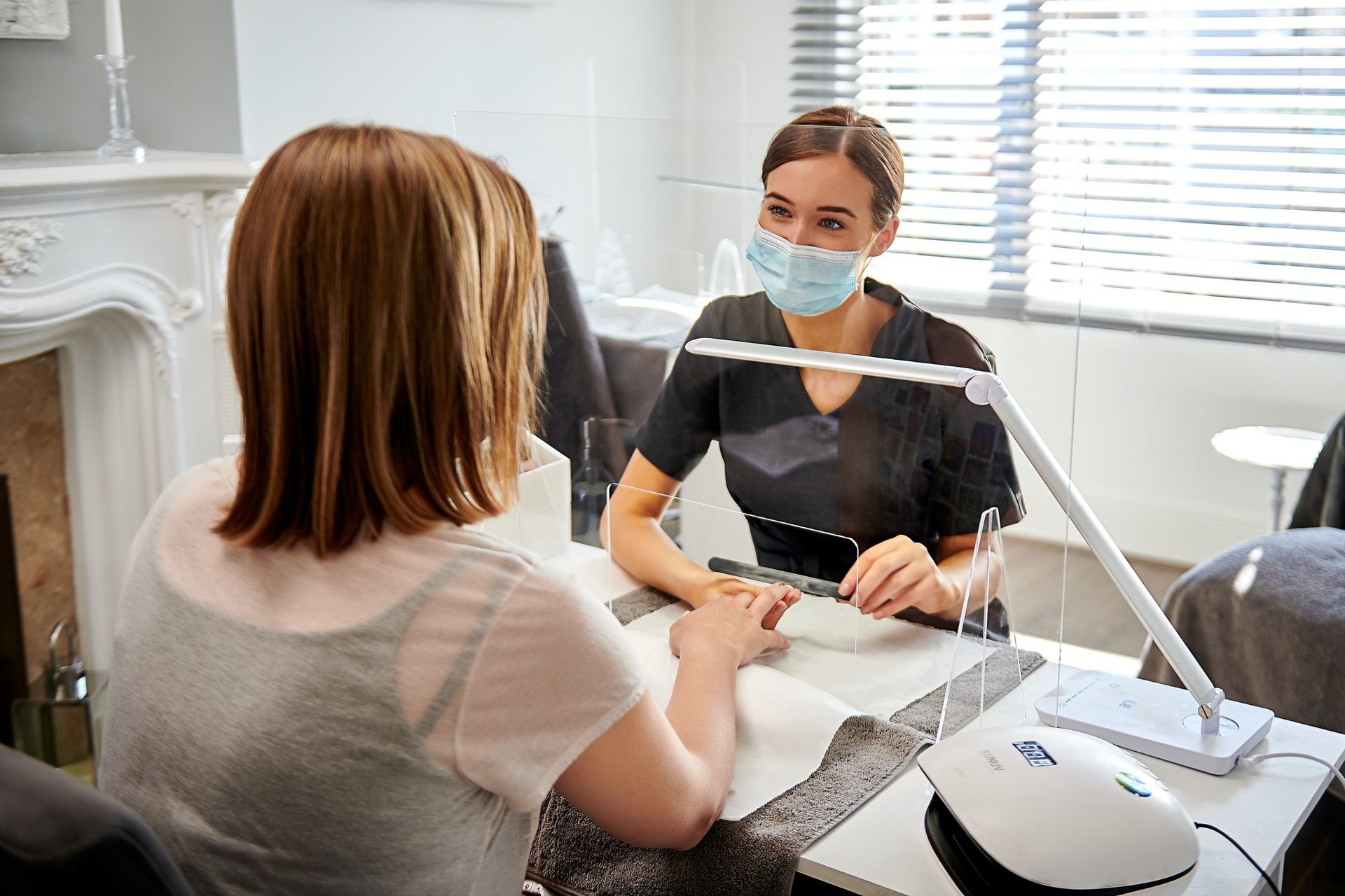 A woman wearing a mask is getting her nails done at a nail salon.