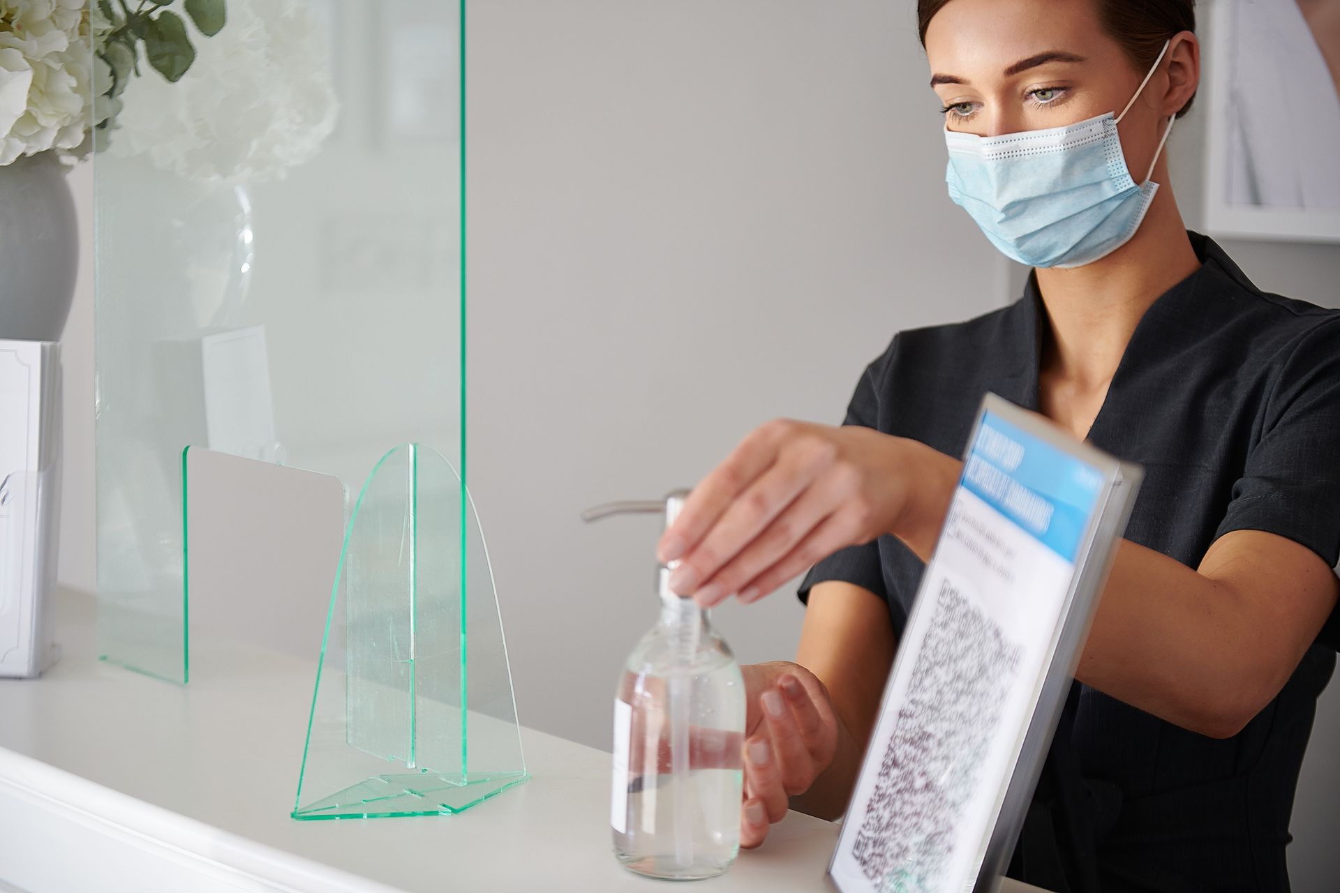 A woman wearing a mask is applying hand sanitizer to her hand.
