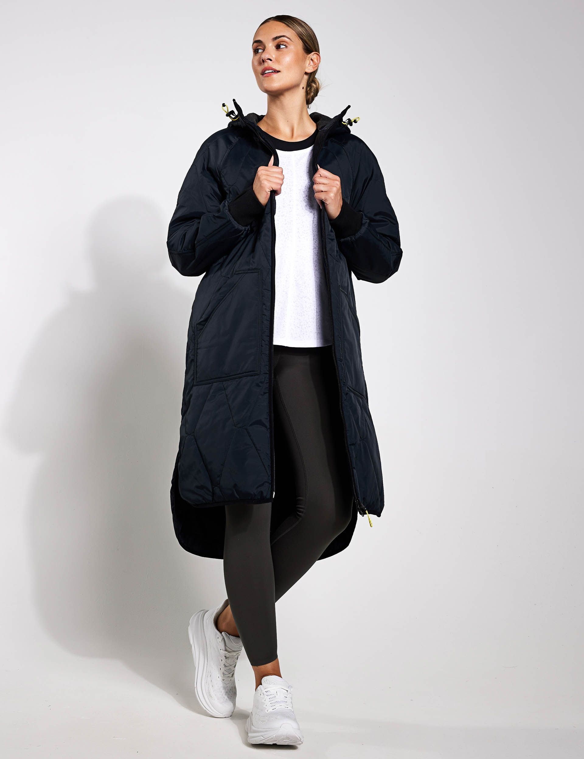 A woman is wearing a long black coat and black leggings.