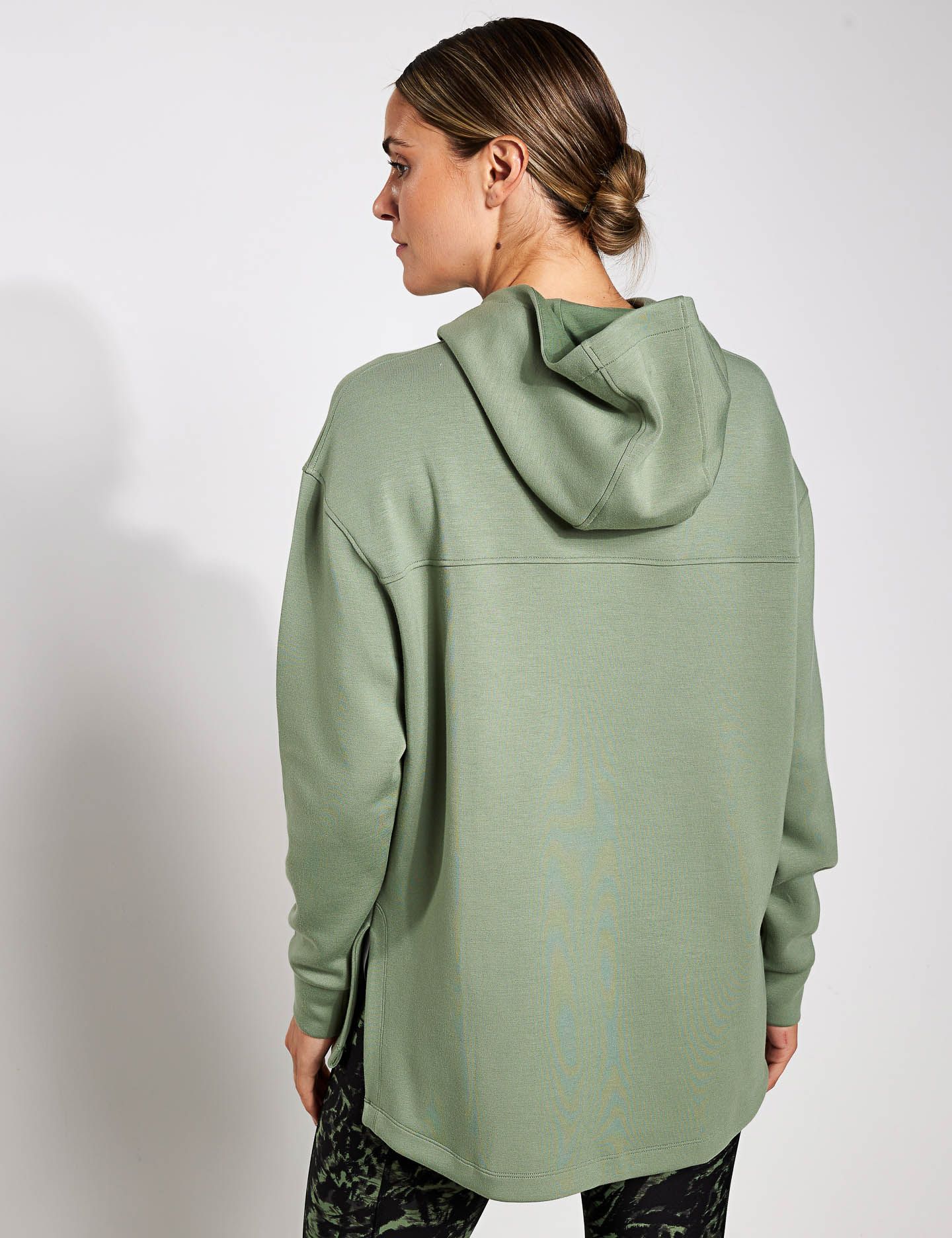 The back of a woman wearing a green hoodie and black pants.