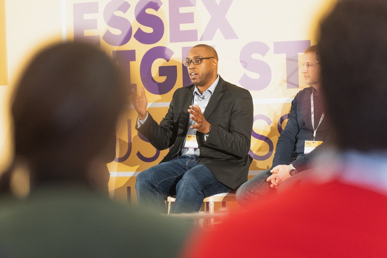 A man in a suit is sitting in front of a group of people and talking.