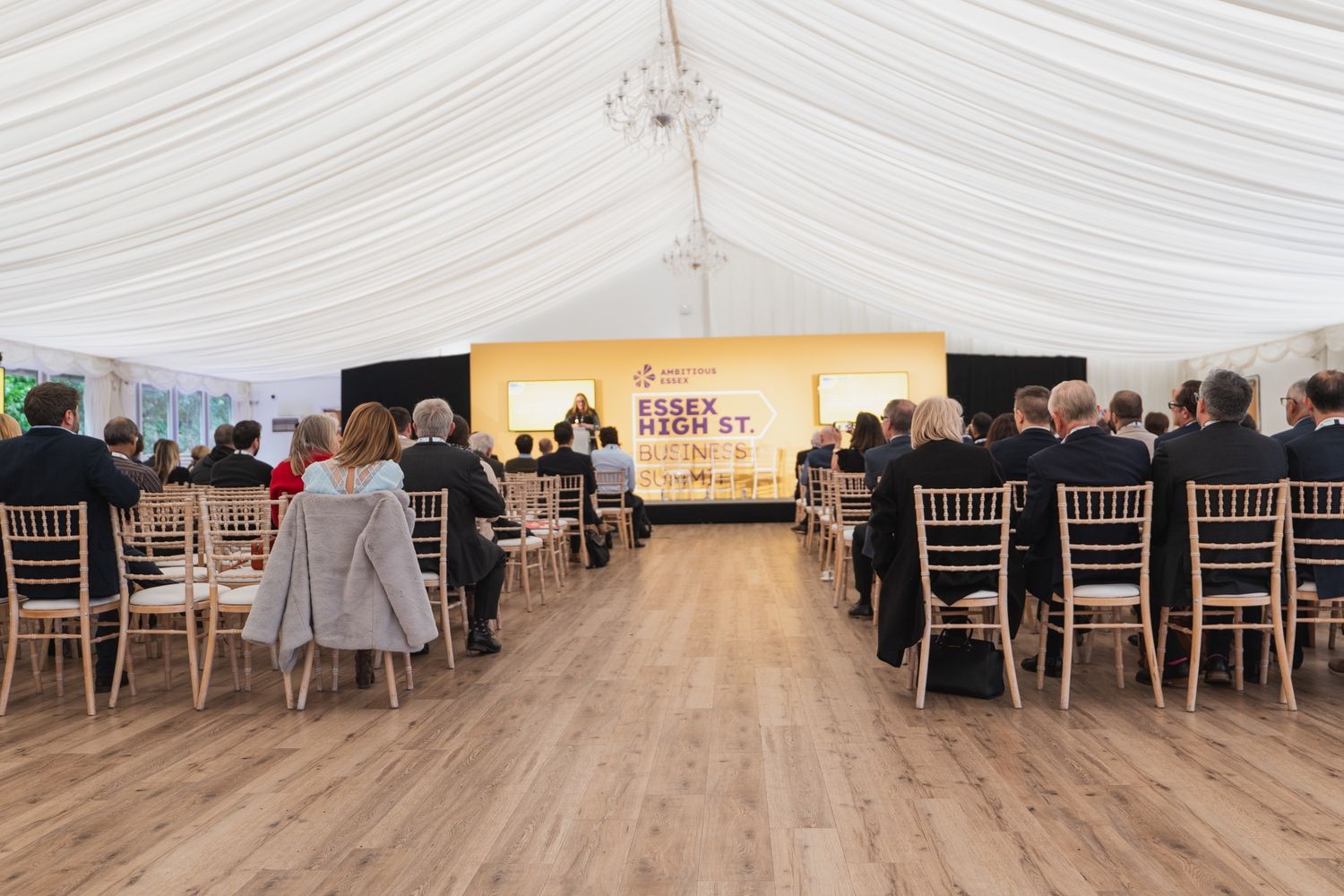 a group of people are sitting in chairs under a tent watching a presentation .