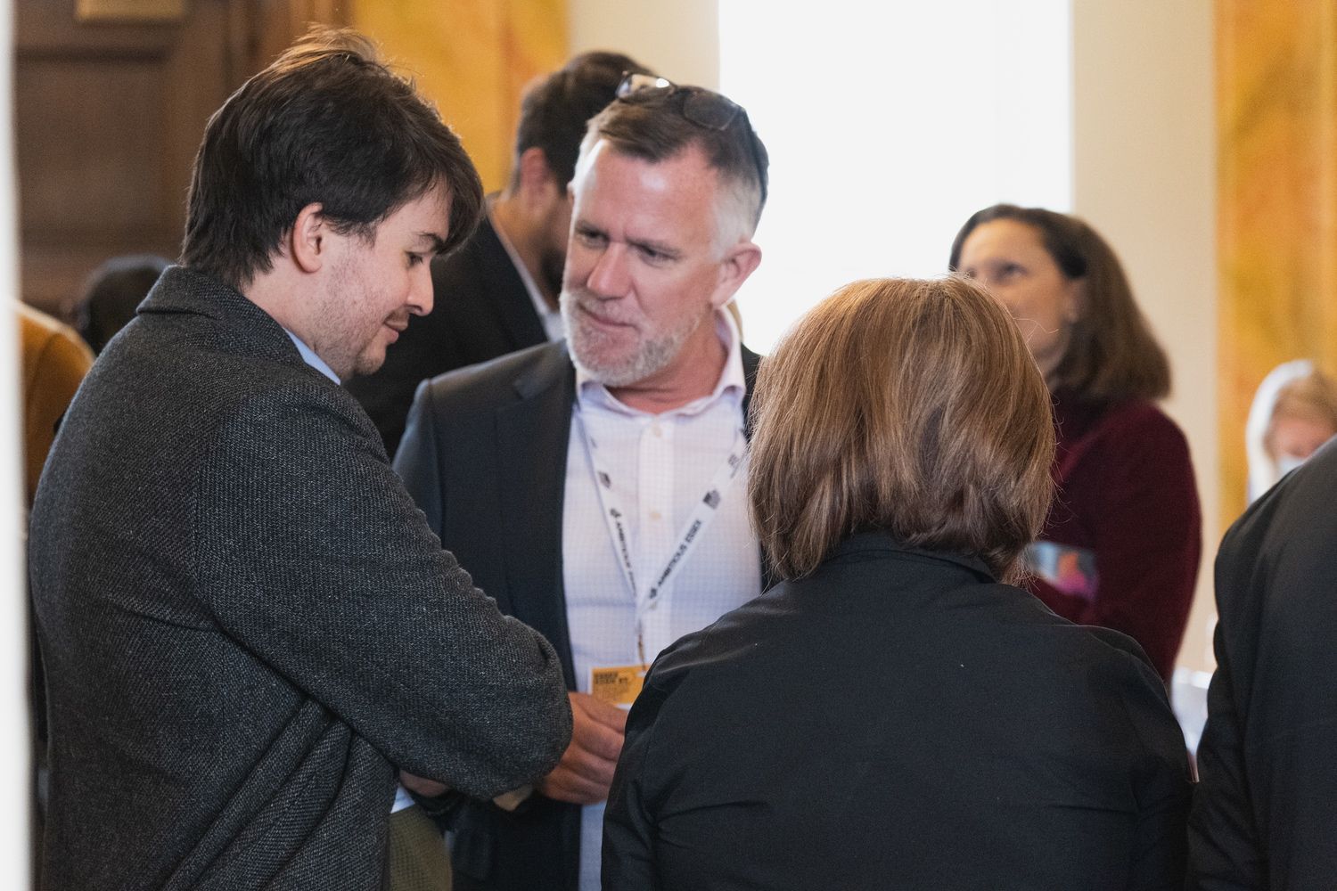 a group of people are standing in a room talking to each other .