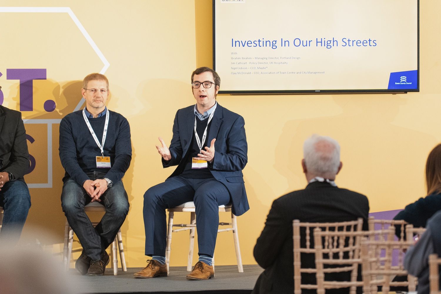 a man in a suit is sitting on a stage talking to a group of people .