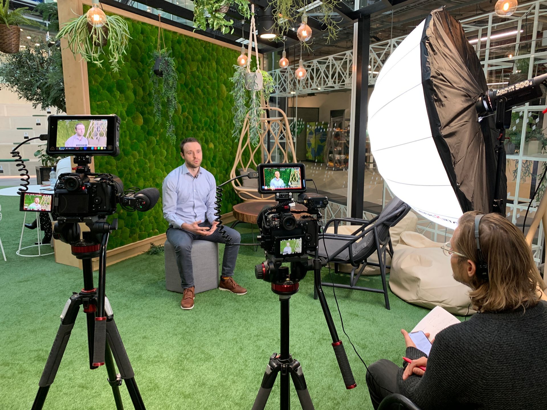 A man is sitting in front of a camera while a woman records him.