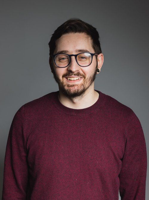 A man with a beard and glasses is wearing a maroon sweater.