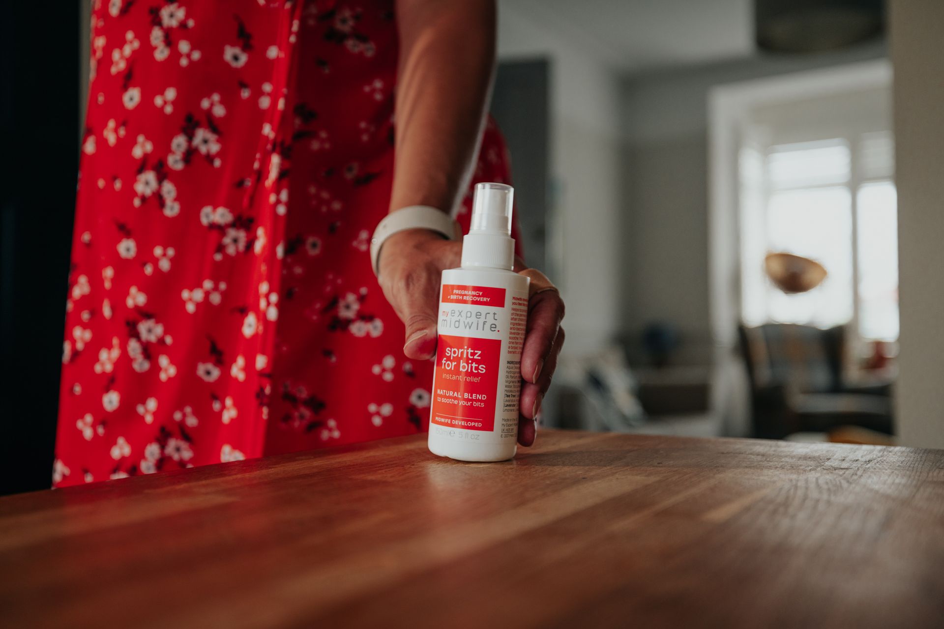 A woman in a red dress is holding a spray bottle on a wooden table.