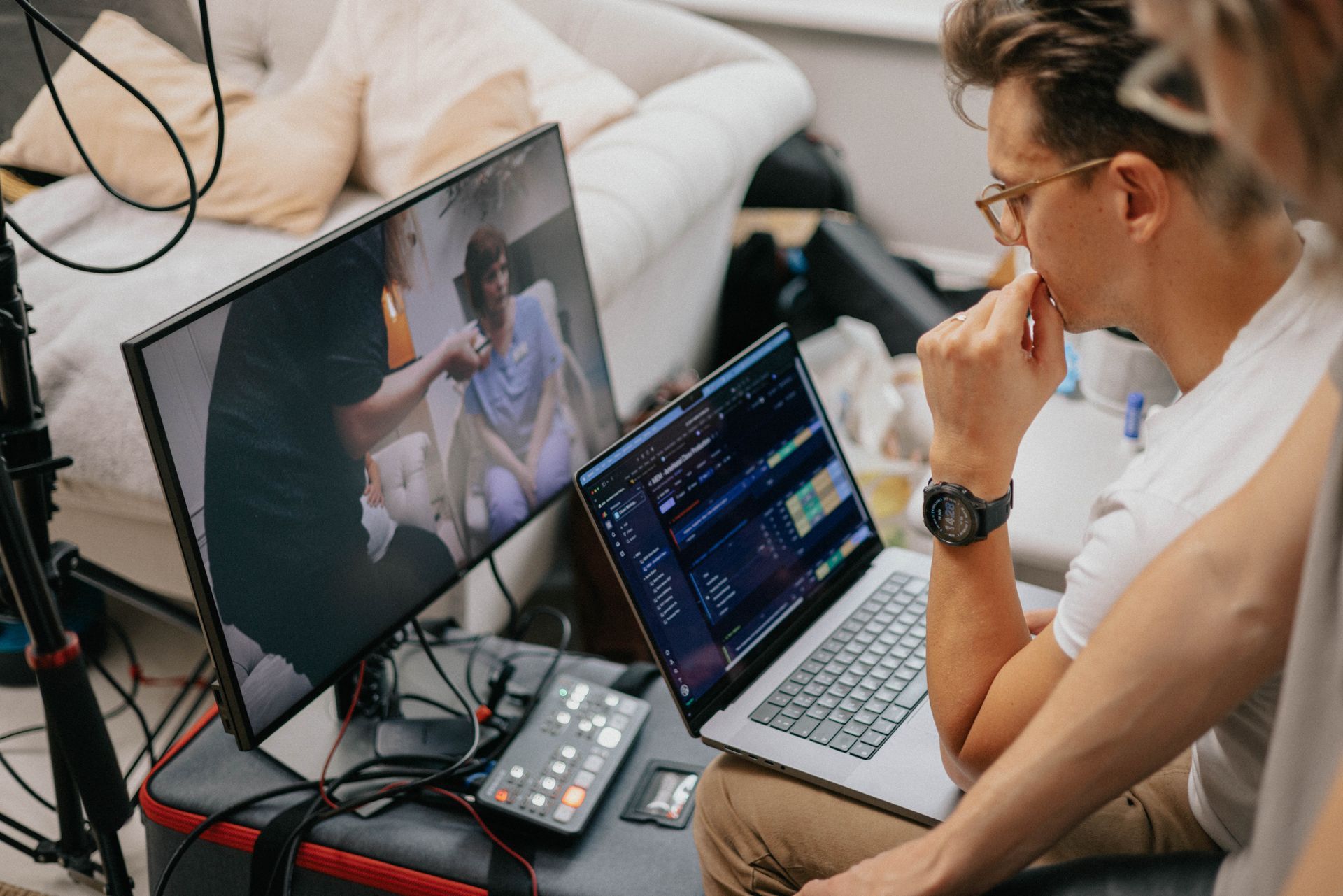 A man is sitting in front of a laptop computer and a monitor.