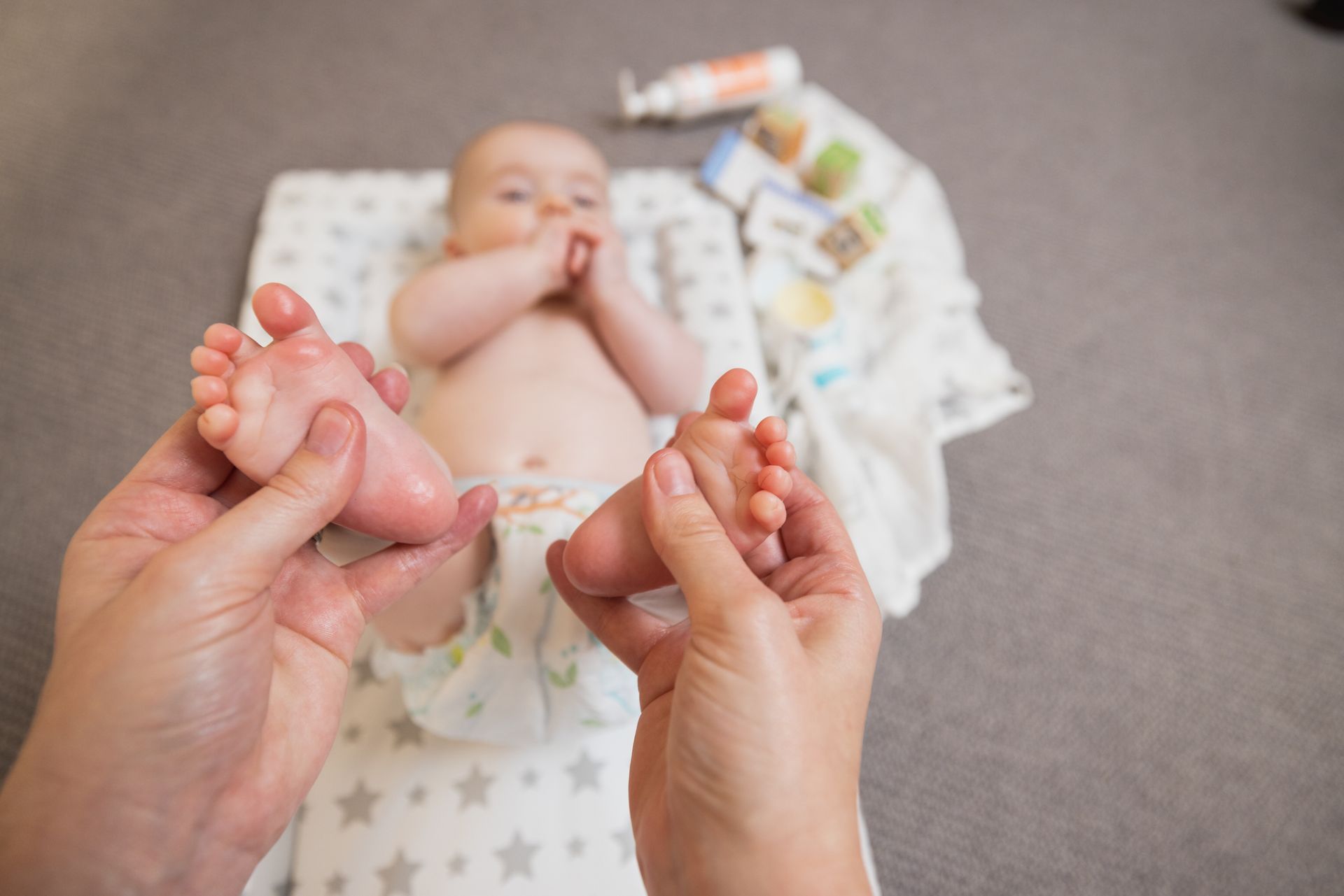 A woman is giving a baby a foot massage while the baby is laying on a blanket.