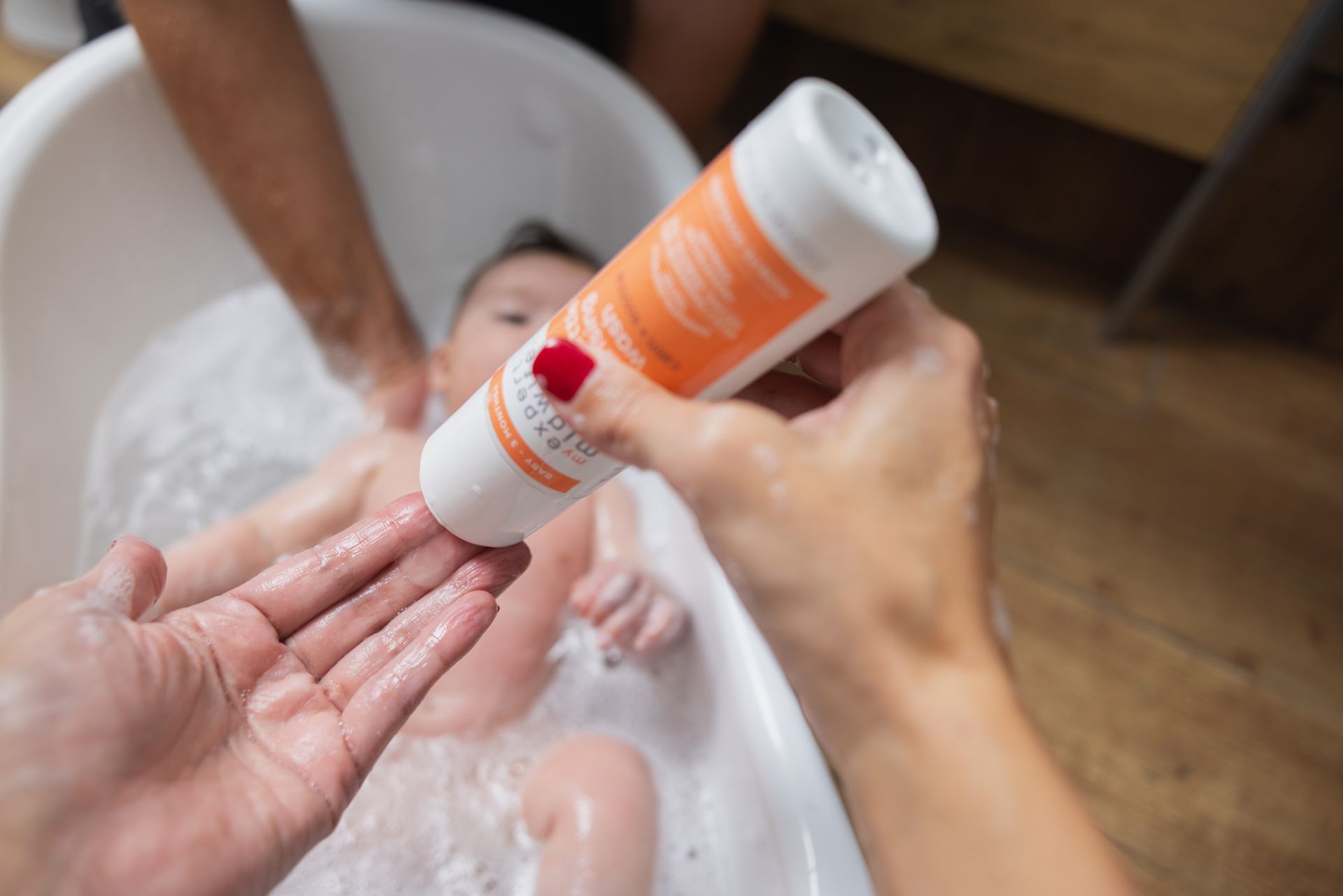 A person is applying lotion to a baby in a bathtub.