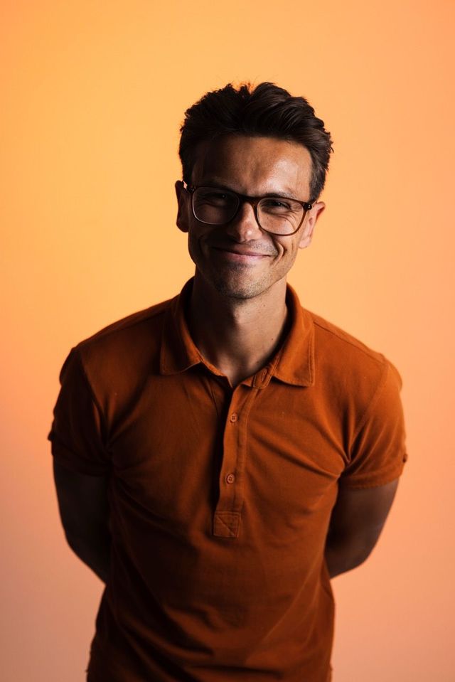 A man wearing glasses and a light blue shirt is smiling for the camera.